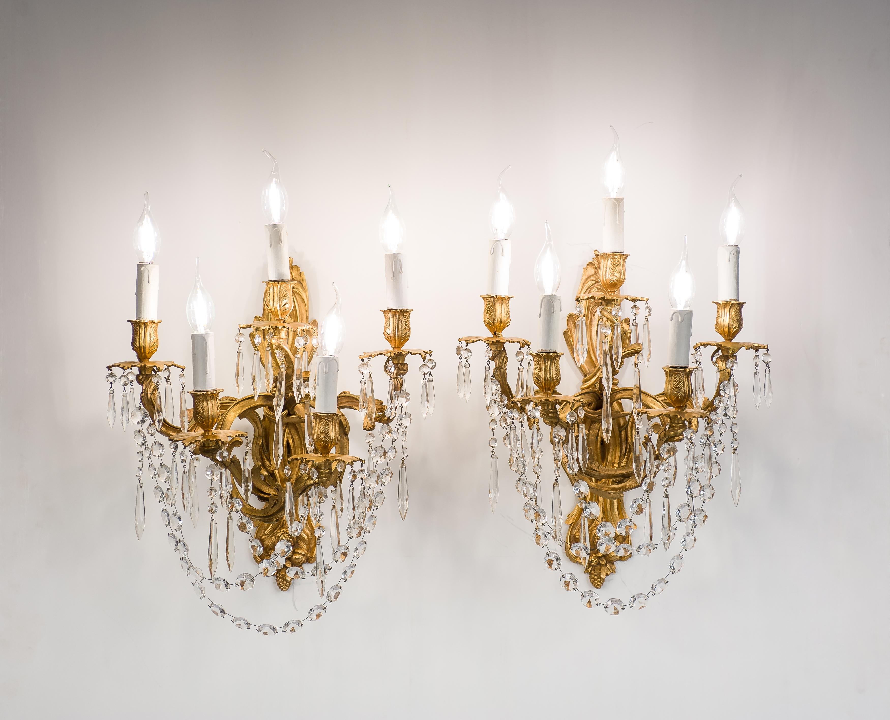 On offer here is a beautiful pair of late 19th-century French bronze fire-gilt and crystal-hung sconces. The large cast bronze sconces each feature five scrolled arms and are decorated with acanthus, scrolls, and floral themes. The asymmetrical