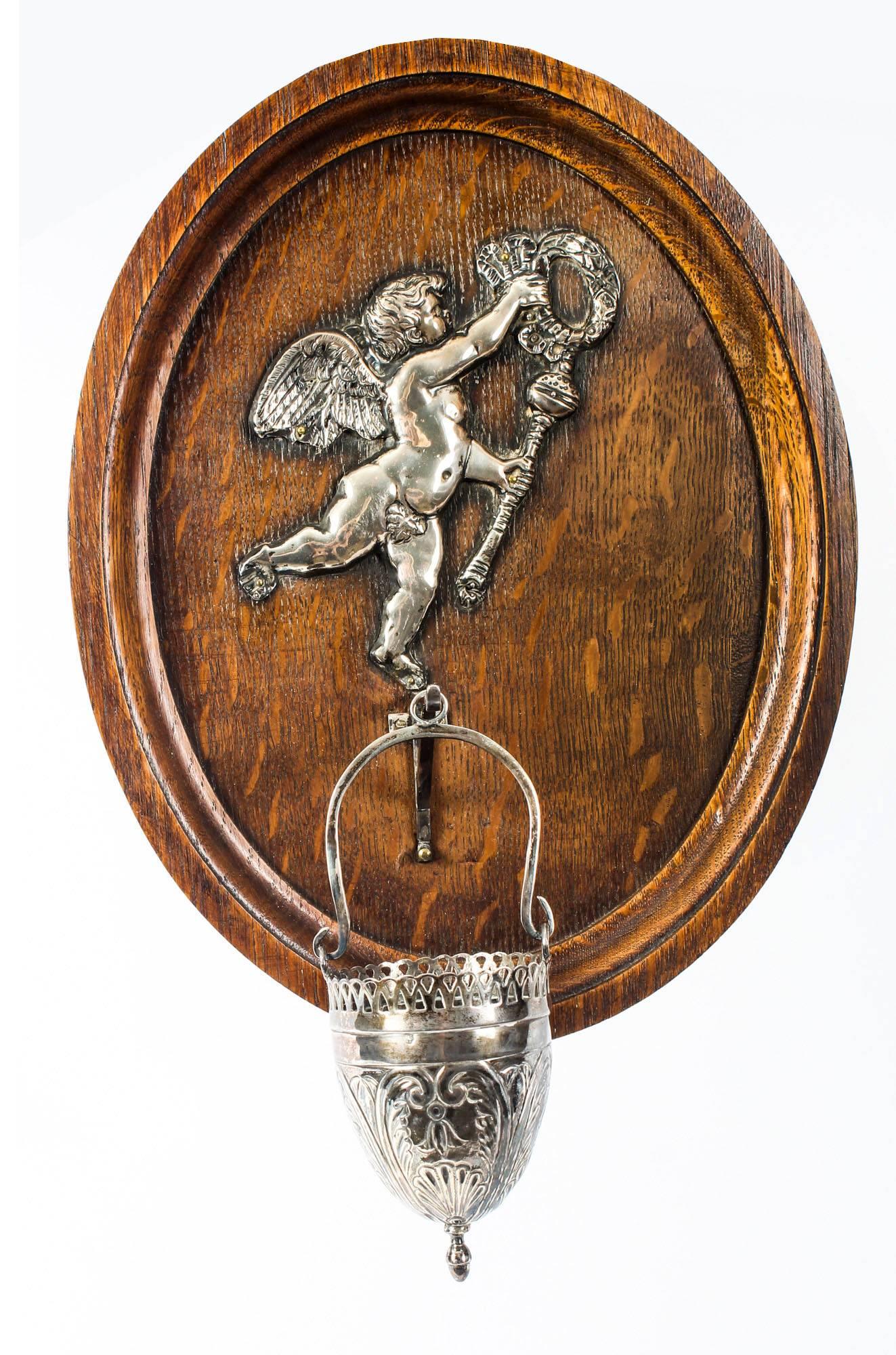This is a beautiful 19th century pair of French wall-mounted holy water stoops.

The oval oak back panels are mounted with decorative silver plated winged cherubs with wreaths each carrying a mace, the water stoops on suspended