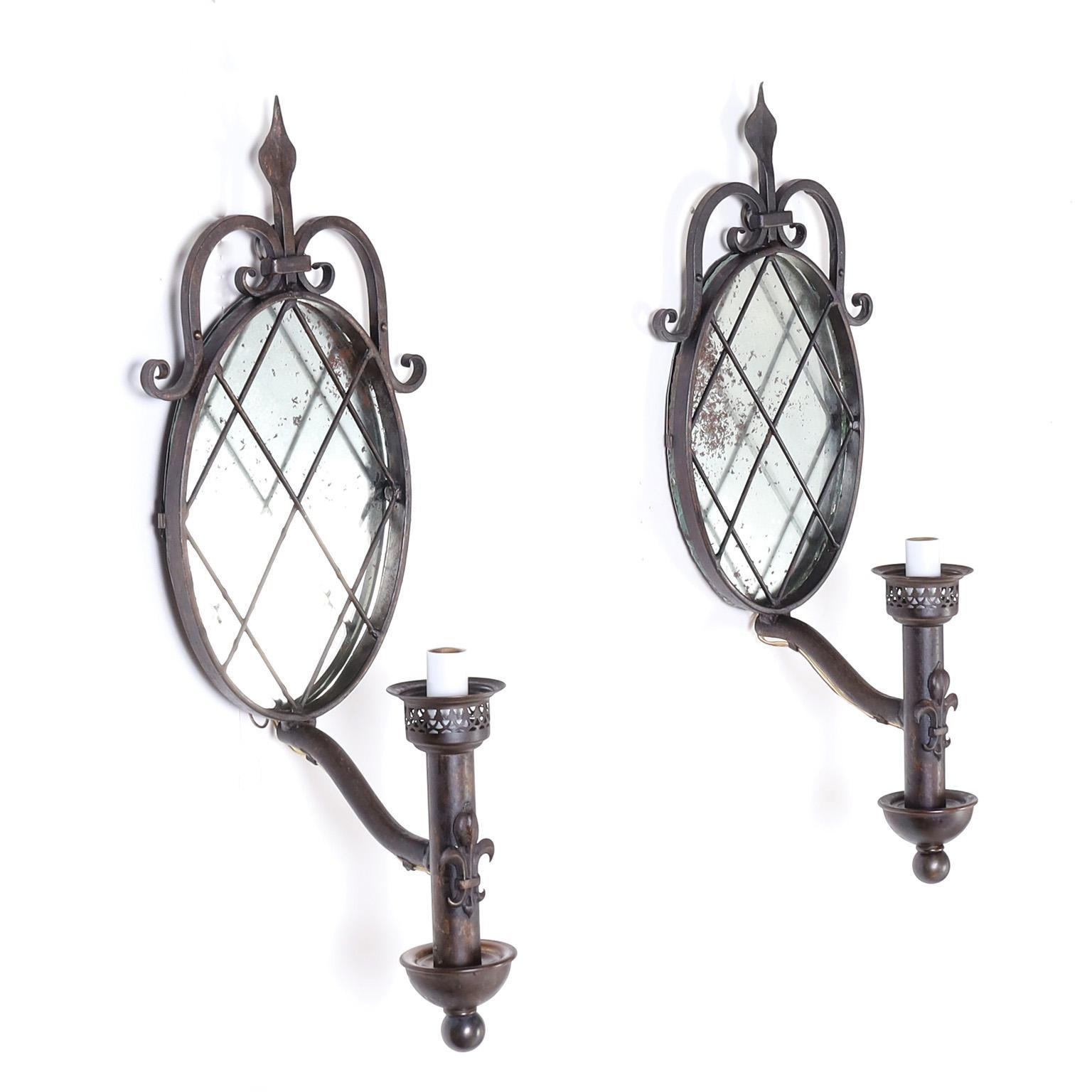 Charming pair of French antique wall sconces with hand wrought scrolled backplates with distressed mirror over metal one light arms with fleur de lis .