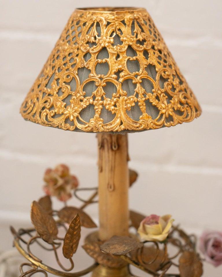 This stunning pair of small antique French bronze lamps with porcelain flowers feature unique silk and metal shades. Placed on a desk or side table, these delicate lamps add whimsy and complete an area.