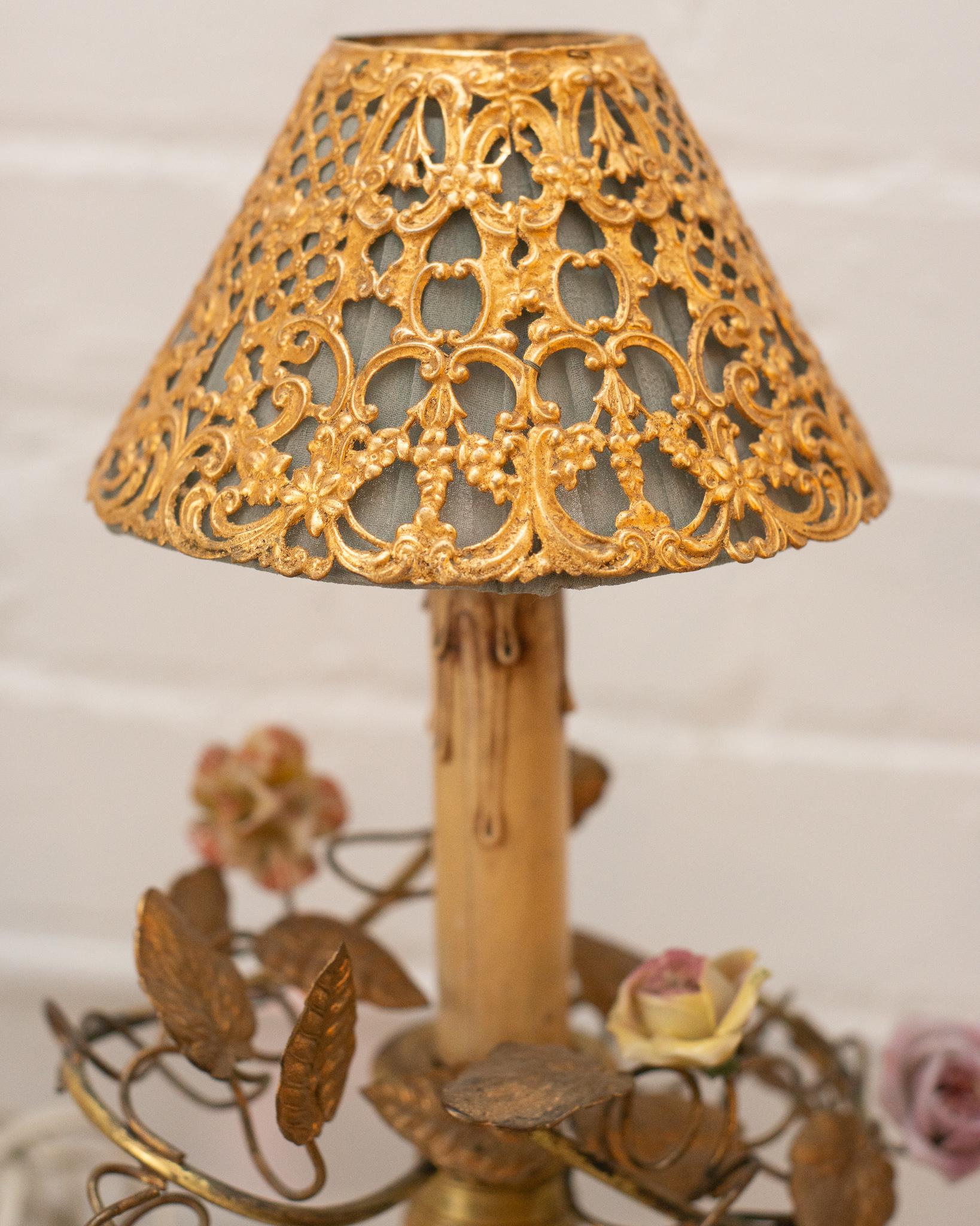 This stunning pair of small antique French bronze lamps with porcelain flowers feature unique silk and metal shades. Placed on a desk or side table, these delicate lamps add whimsy and complete an area.