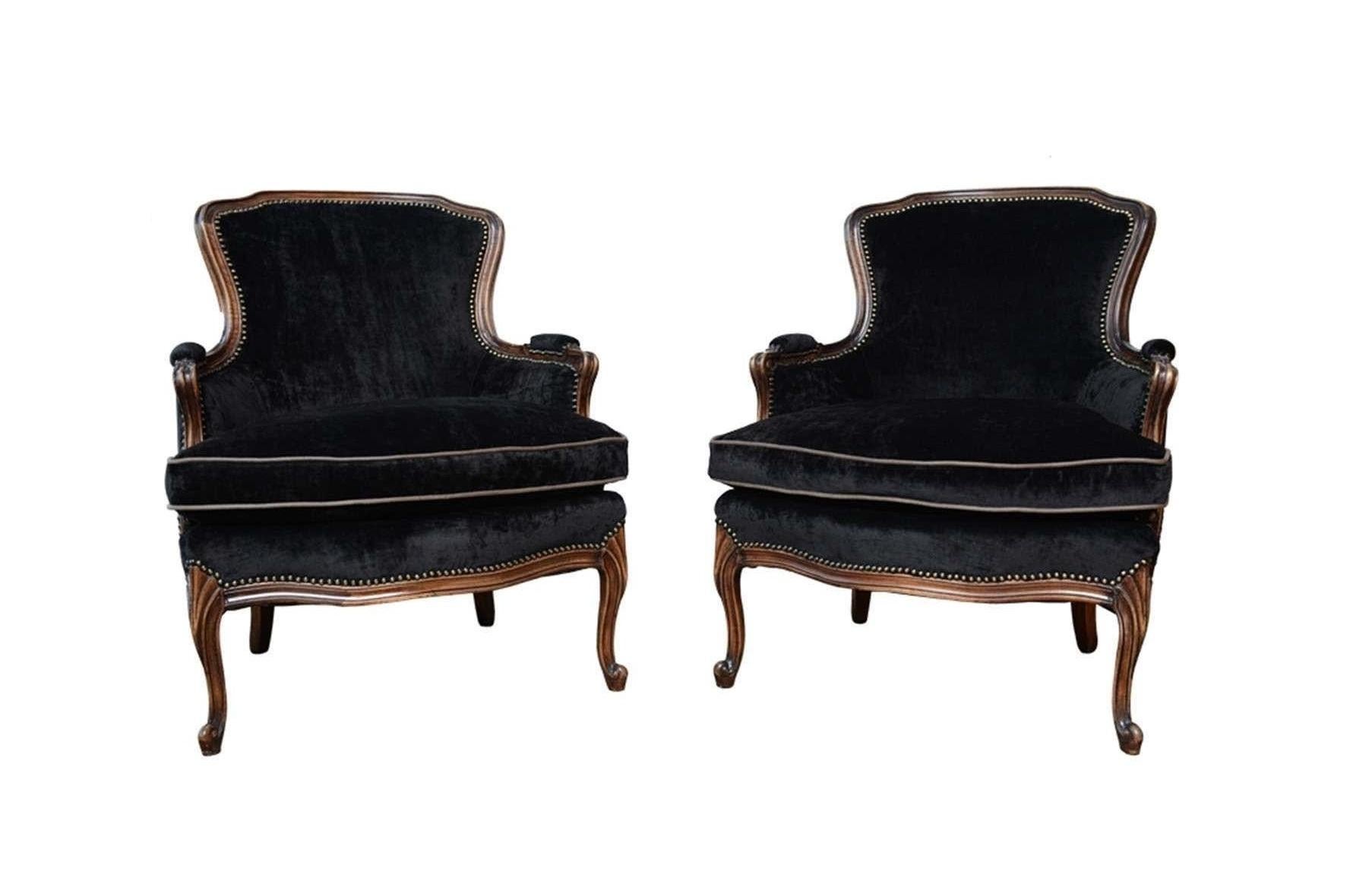 An elegant pair of antique Louis XV upholstered arm chairs. Freshly upholstered in a black velvet with nailhead trim bordering the edges and the frames refinished in a dark walnut finish. The chairs feature a simple curved crest rail, upholstered