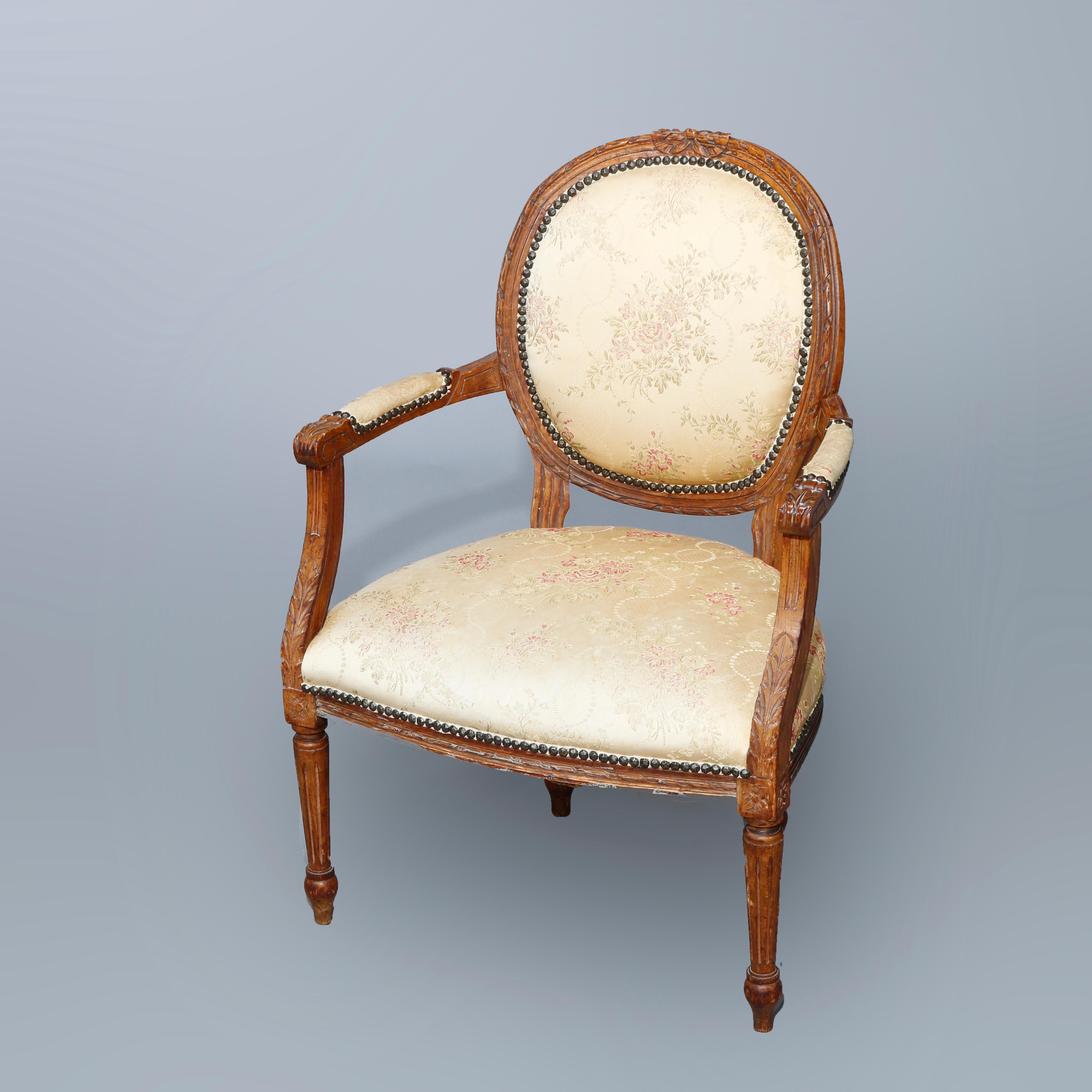 An antique pair of French Louis XVI style fauteuil armchairs offer caved walnut frame with foliate crest surmounting medallion form upholstered back, raised on reeded and tapered legs, 19th century.

Measures: 34.75