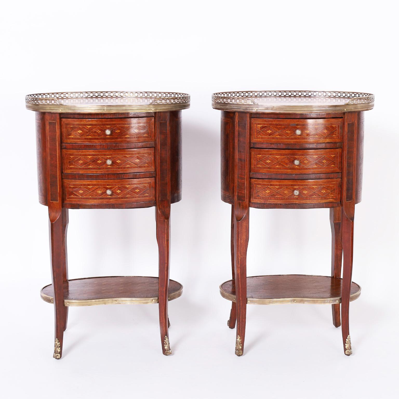 Refined pair of antique French Louis XV style stands with rouge marble tops having a brass gallery over a three drawer case with brass hardware, cross banding and ebony and kingwood classic inlays. The four elegant legs are connected by a kidney