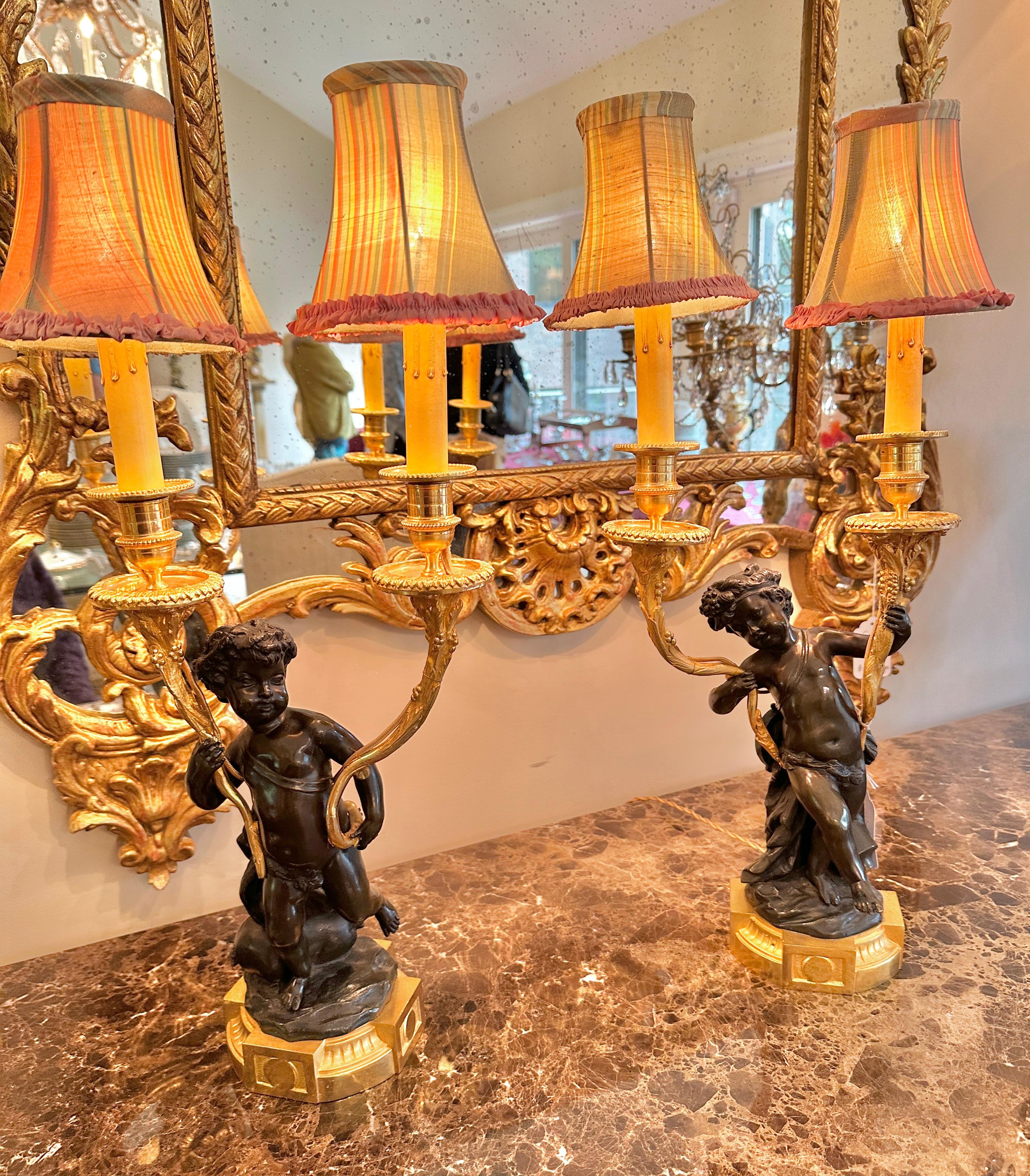 Indulge in a Museum Quality Pair of French Patinated Bronze and Gilt Bronze Cherub Candelabra Lamps with Silk Shades.
This is an exquisite Pair Of Antique French Napoleon III - Belle Epoque Patinated and Dore Gilt Bronze Cherub Putti Candelabra