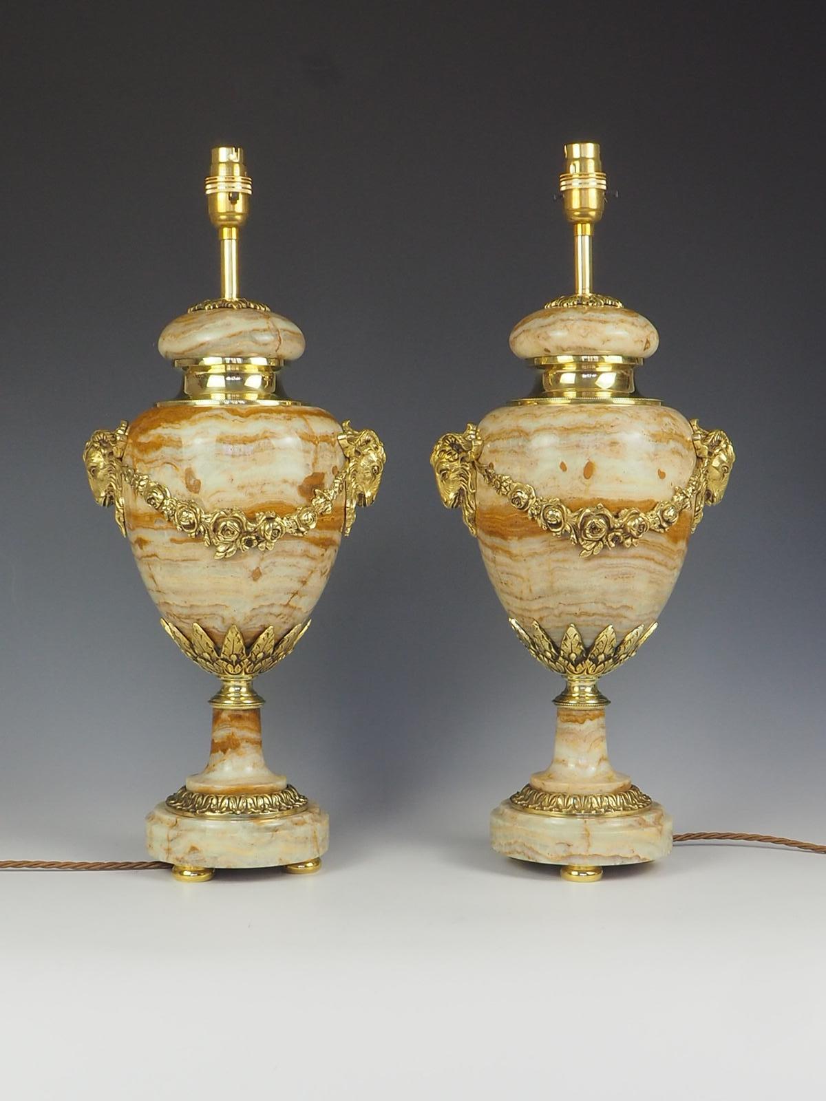Exquisite pair of French Ormolu Cassolette Marble Table Lamps showcases the elegance and craftsmanship of the Louis XVI period.

These lamp feature stunning Ormolu bronze mounts adorned with intricate floral swags and delicate rams heads serving as
