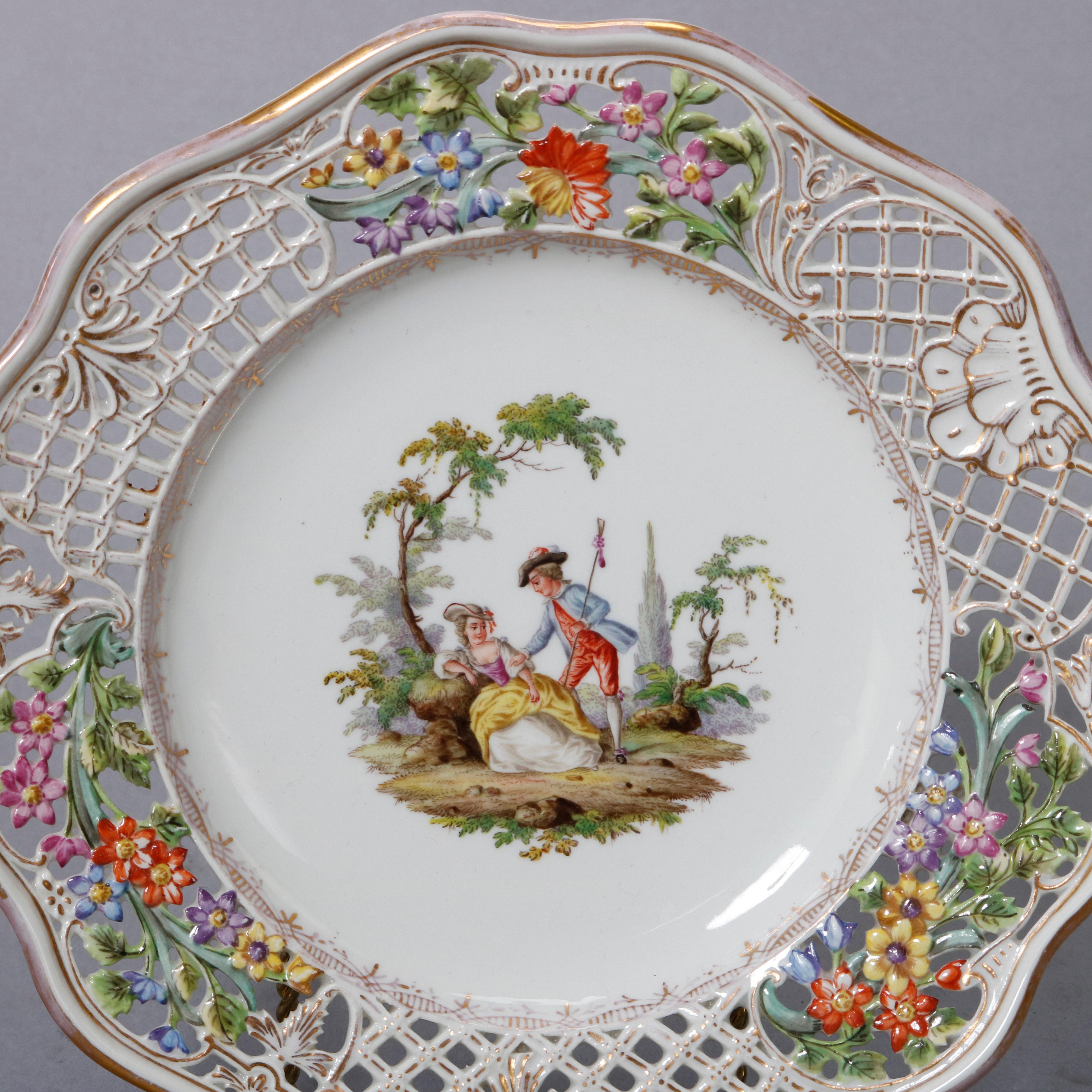 An antique pair of German porcelain plates by Meissen offer central hand painted courting scenes in countryside settings with scalloped and reticulated rim having basket weave pattern with floral reserves, gilt highlights throughout and en verso