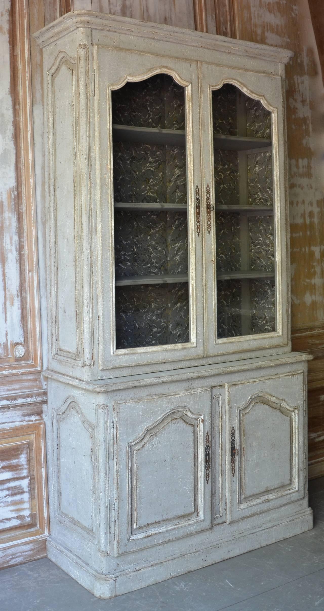 A stunning pair of Gustavian LV style bookcases from Sweden in a light-grey patina finish. The book cabinets have glazed top panels, a base with fielded panel doors and paneled sides. Inside is decorated with lovely papered walls and three