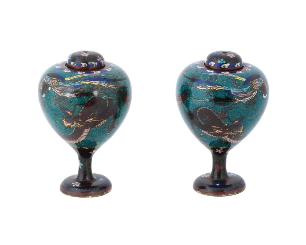 A pair of antique Japanese Early Meiji period vases, characterized by their oval shape tapering downward, mounted on stems, and adorned with matching covers. The surfaces of these vases feature intricate cloisonne enamel work showcasing a dragon