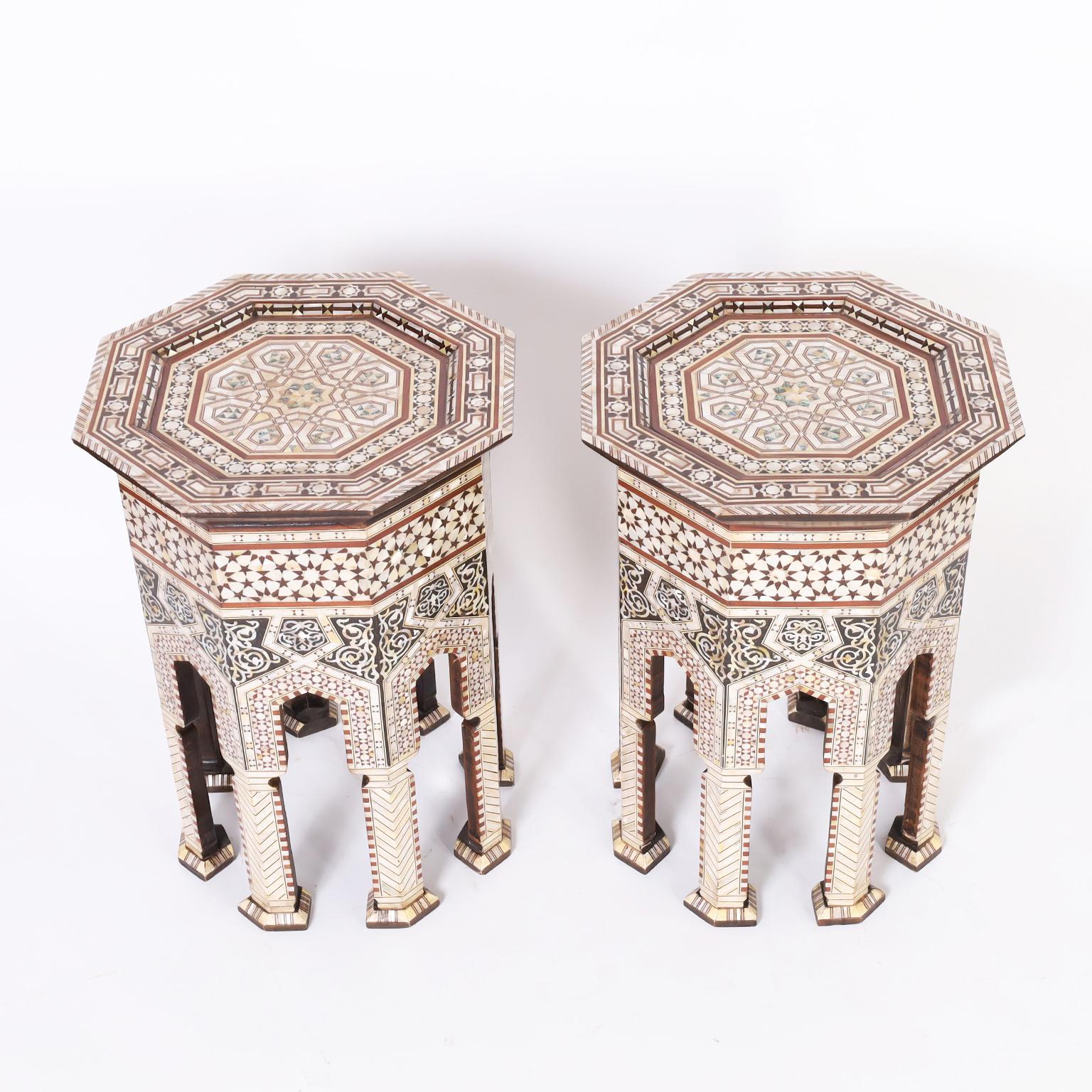 Ultimate pair of Moroccan stands crafted in walnut having octagon tops ambitiously inlaid with geometric designs in mother of pearl, penshell, ebony, and mahogany that continues over the eight sided bases having moorish arches and stylized pad feet. 