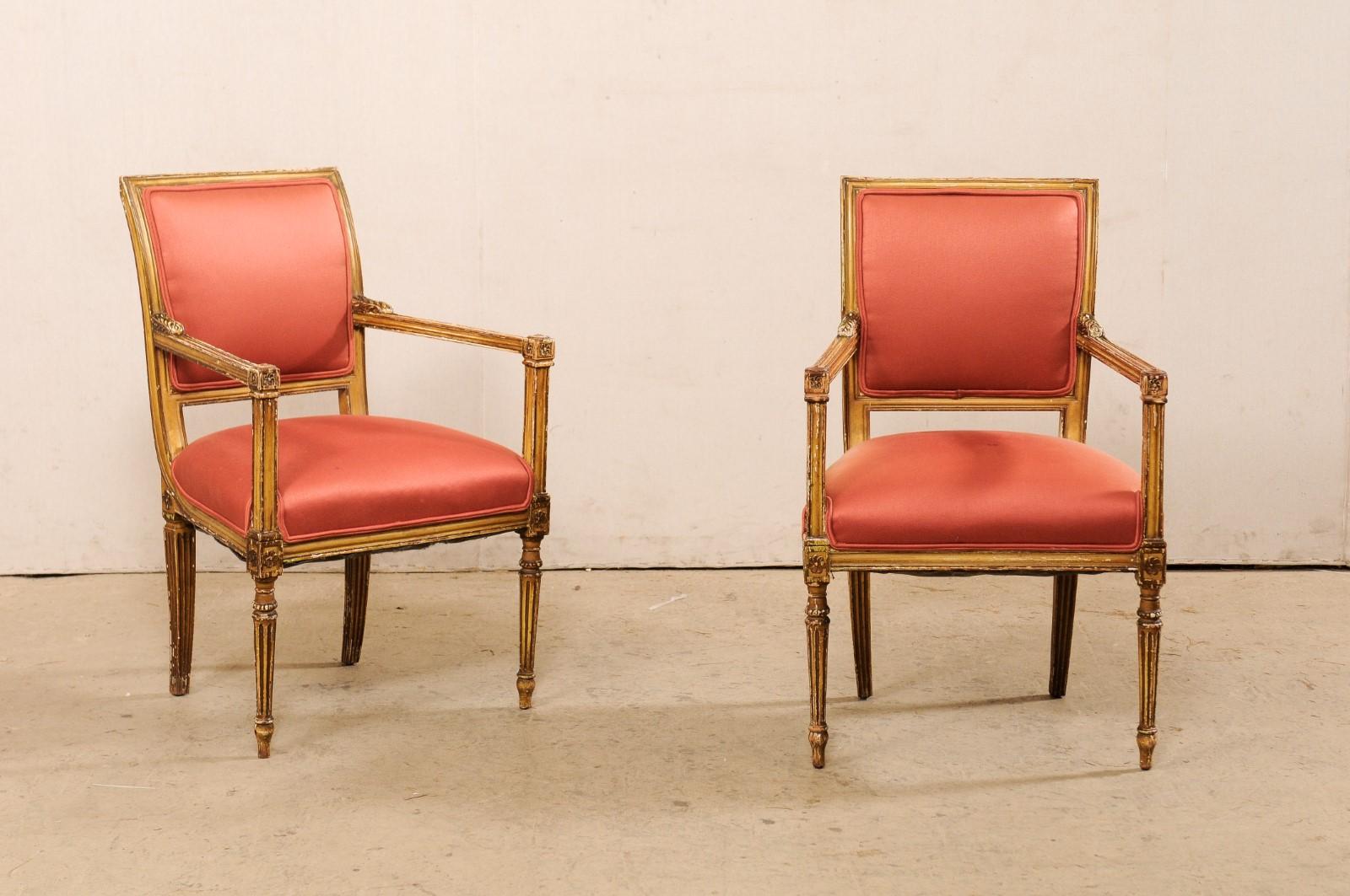 An Italian pair of Neoclassical style armchairs from the early 20th century. This antique pair of accent chairs from Italy are each carved with neoclassic stylings with clean/linear arms topped with acanthus leaves carved next to the back rest and