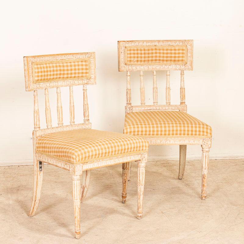 Charming pair of Swedish gustavian chairs. Note the traditional carving and fluted legs and distressed white paint that has come through generations of use, softening the look which compliments the style and grace of this pair. The taupe checked