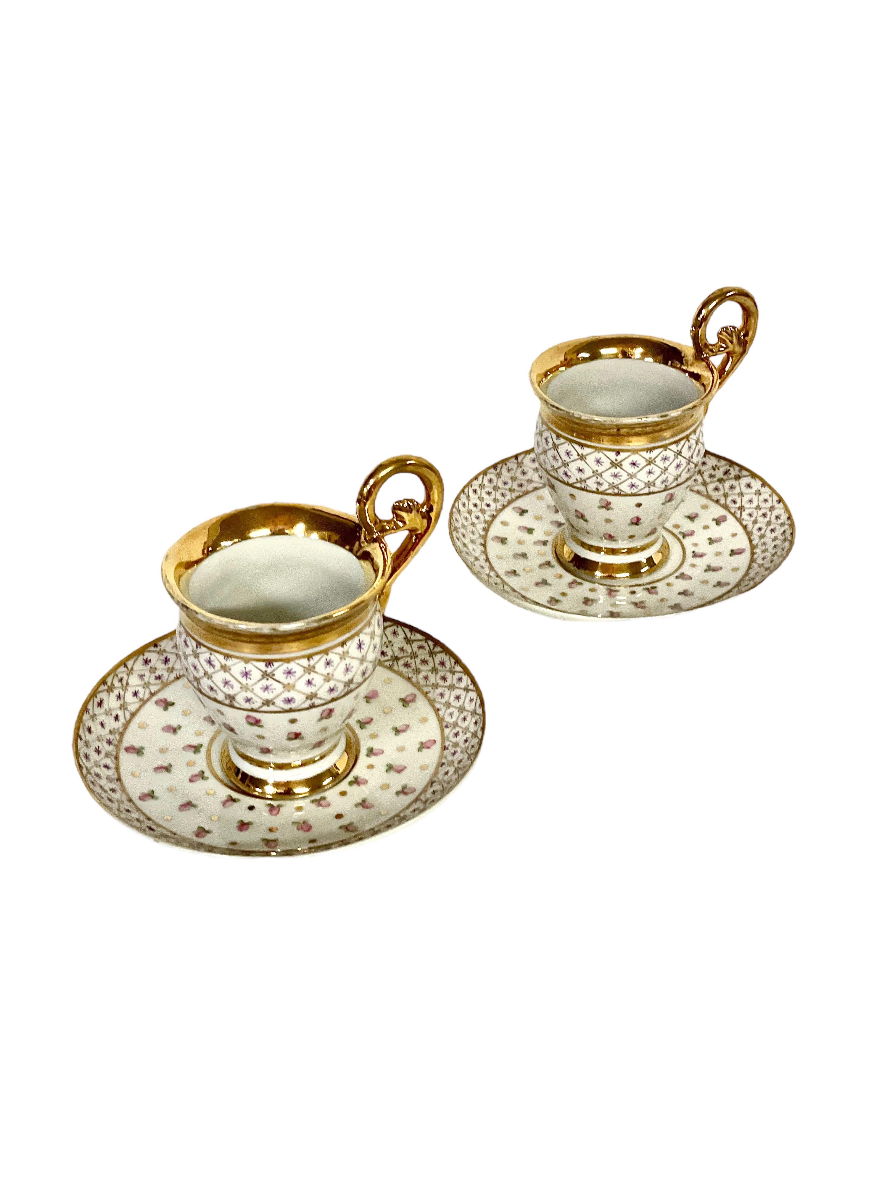 An exquisite pair of antique white 'Porcelaine de Paris' teacups and saucers, intricately hand- painted with gilt decoration throughout. Dating from the early 19th century, the cups have characteristically high, curved handles, which, like the cup