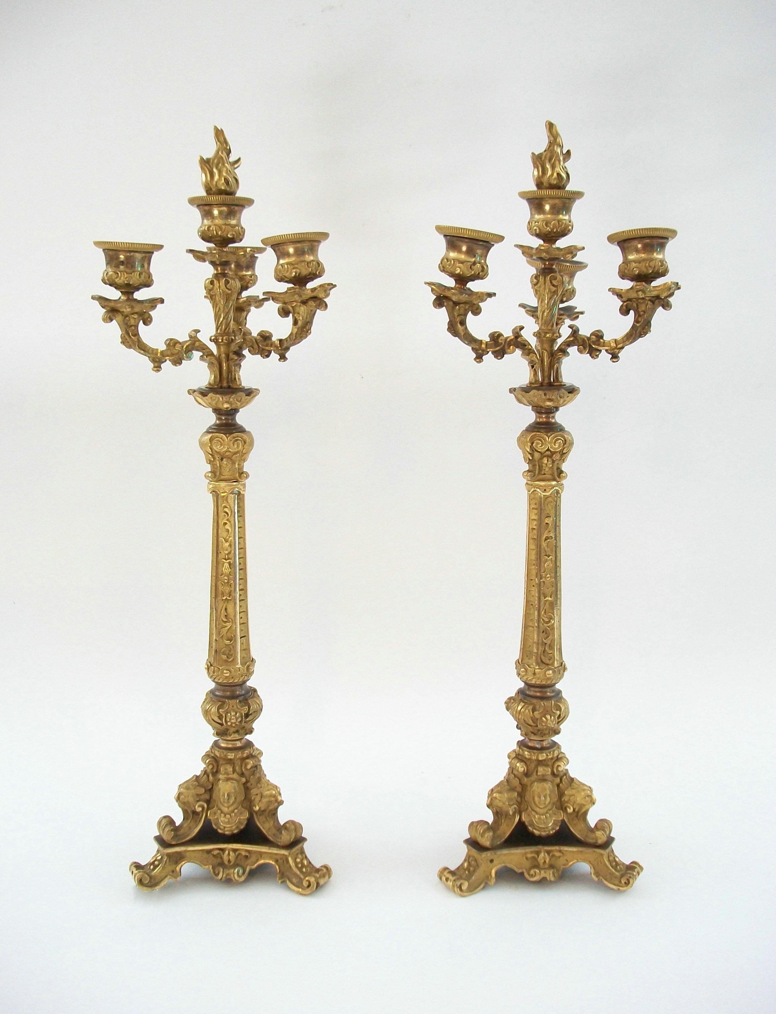 
Antique pair of Restoration period gilt bronze candelabra - featuring elaborate Neo Gothic bronze castings of masks, lions and scrolls on trefoil bases with hand hammered and chiseled details topped off with fire gilt highlights - original patina