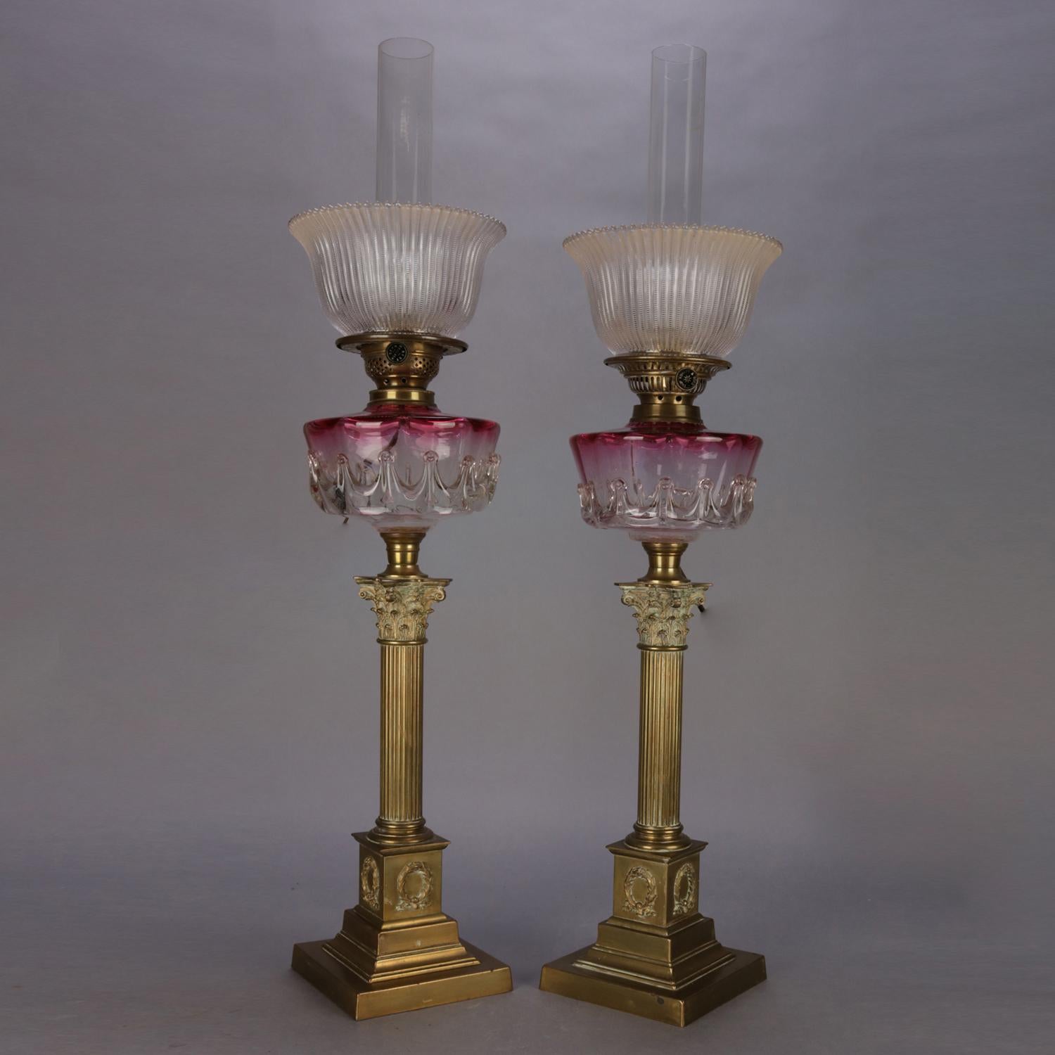 An antique pair of electrified oil parlor lamps feature rubina glass fonts with crown form design and raised on Corinthian column form bases, professionally rewired, circa 1840.

Measures: 34