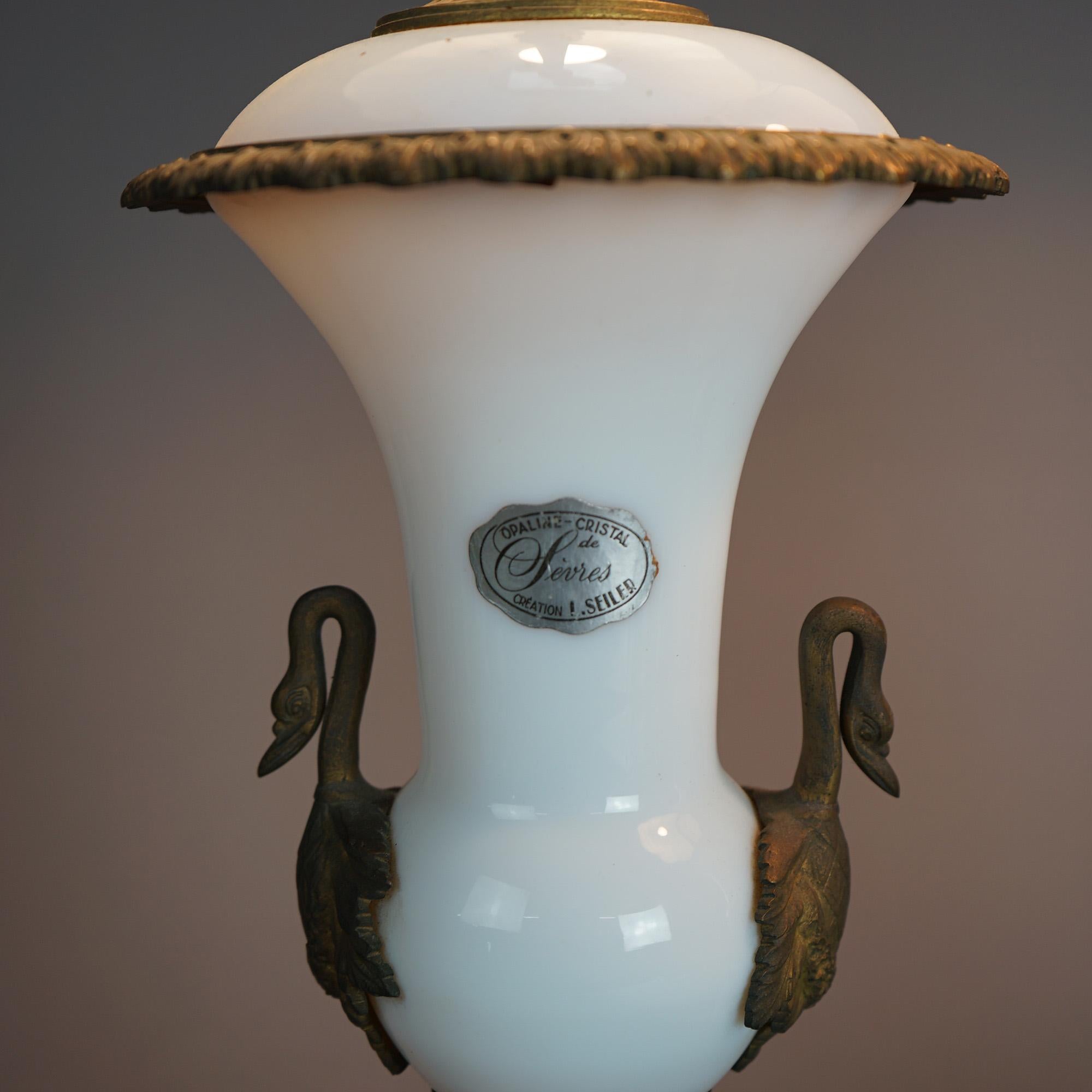 An antique pair of Sevres French opaline table lamps offers glass urn form bases having cast bronze mounts to include double figural swan handles; maker label as photographed; c1920

Measures - 34.25