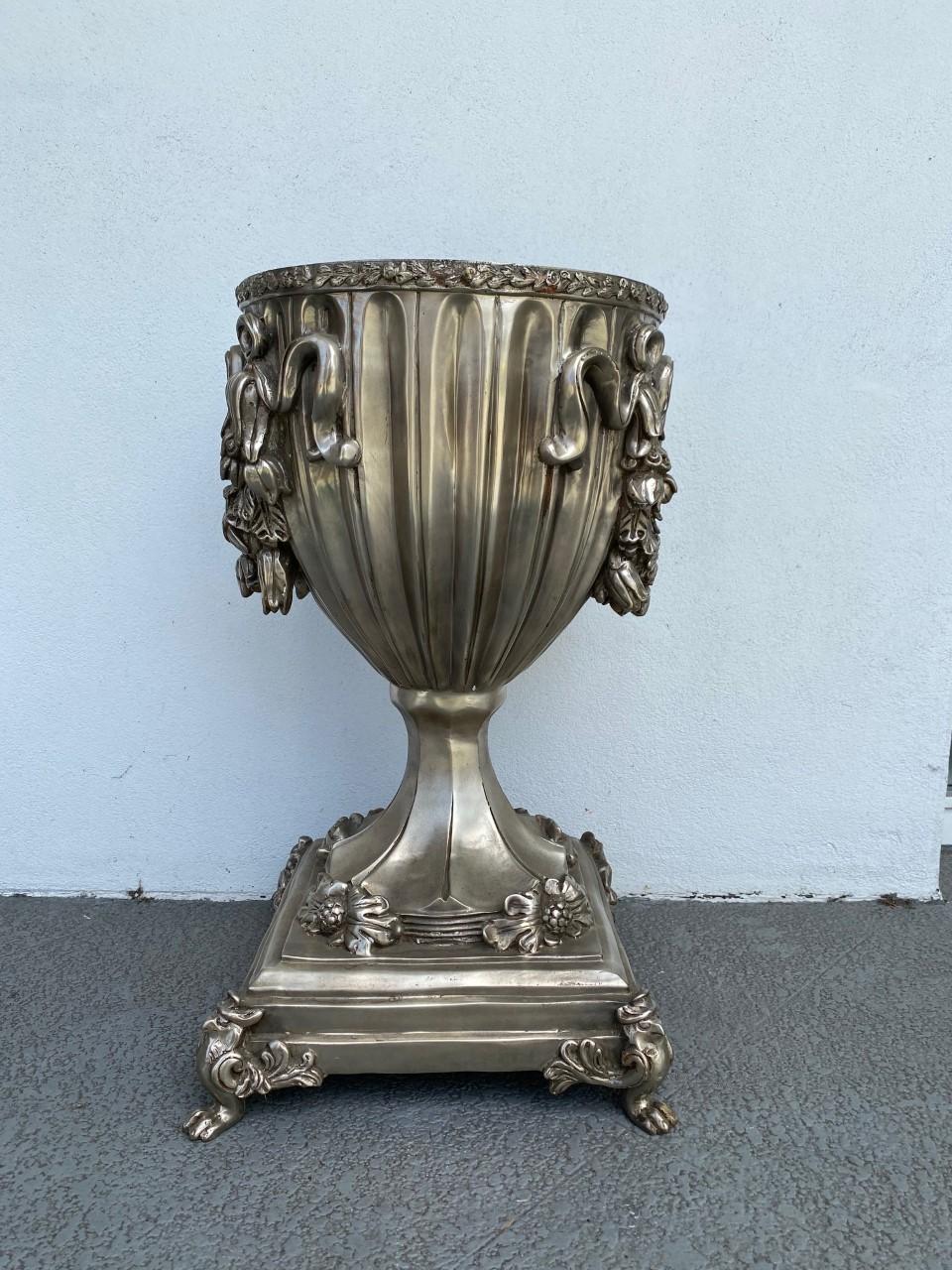 Beautifully classic, this luscious pair of silver dipped bronze urns bring an element of elegance. Each piece is full of meticulous detail. When looked up close, the silver dipped bronze details of ribbons, foliage, flowers and mythological animal