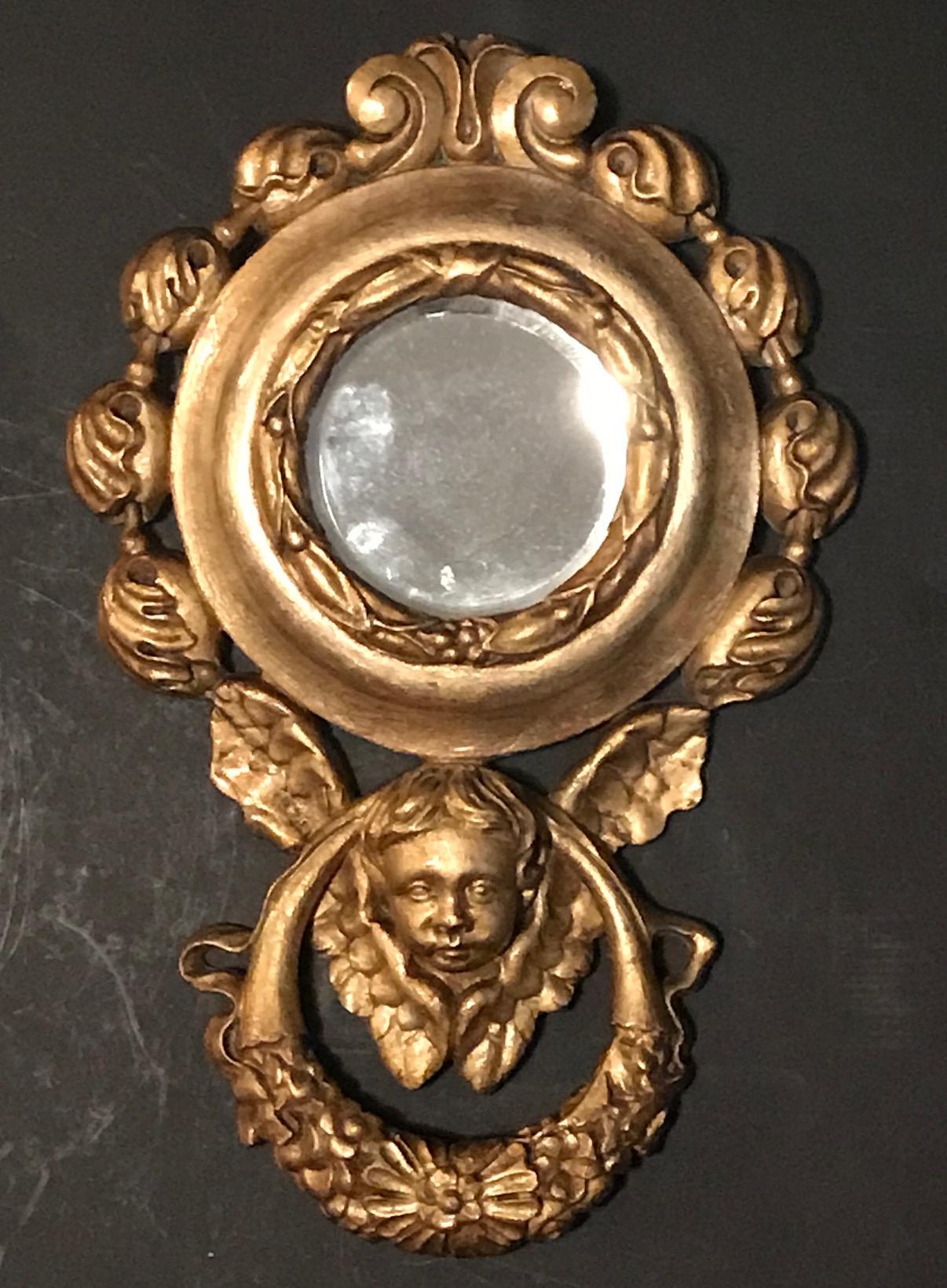 This is a beautiful pair of hand carved and gilded wall mirrors. They are created around the turn of the century. The mirrors in a circular shape are surrounded with carved floral ornaments. A winged putto inside a garland is on the lower end of