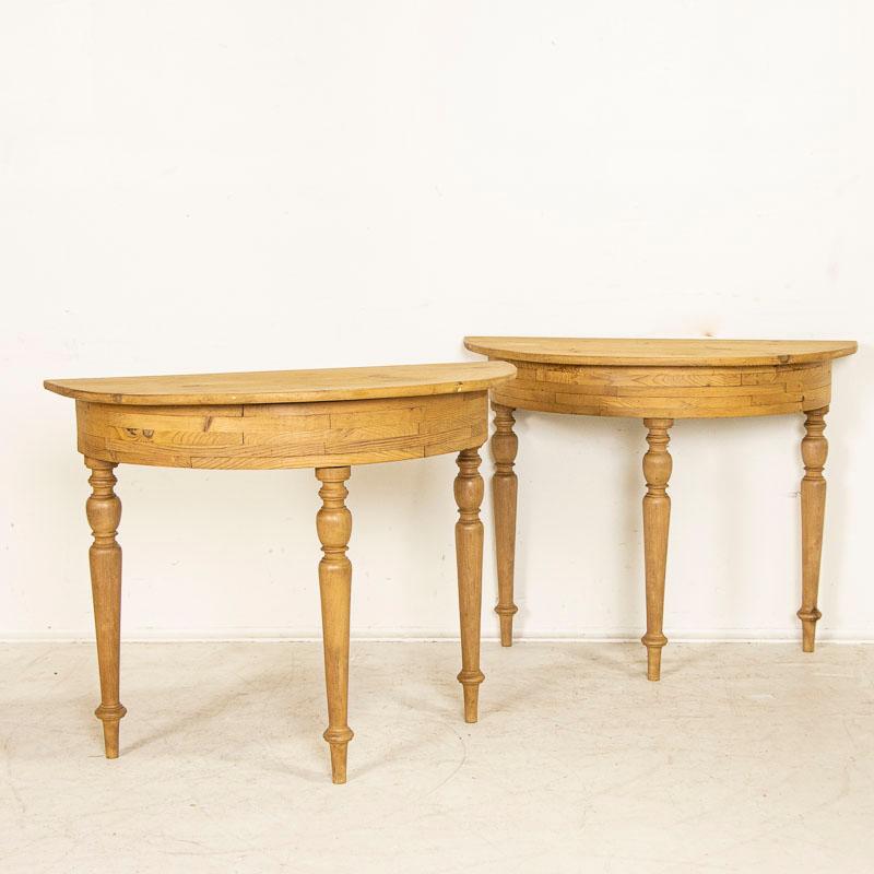 The natural pine of these Swedish demi-lune tables has been waxed, bringing out the warmth of the wood. Please examine photos to appreciate the turned legs and layered details of the table skirt. The old knots, dried out worm holes and signs of wear