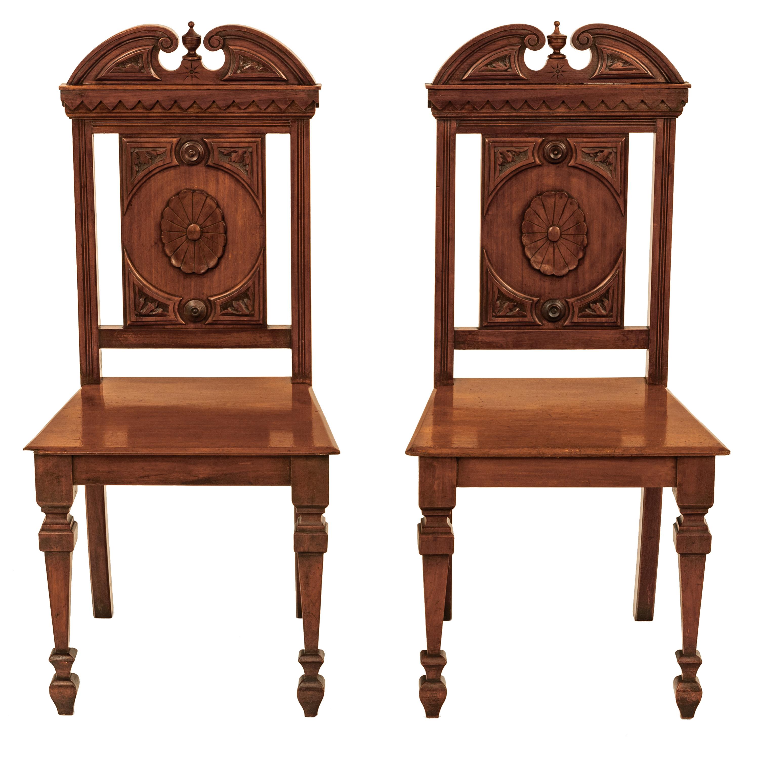 A good pair of antique Regency carved mahogany hall chairs, in the Neo-Classical style, 1830's.
The chairs having an architectural twin 'Swan's Neck' pediment to the top & flanking a turned urn shaped finial, each chair back having central carved