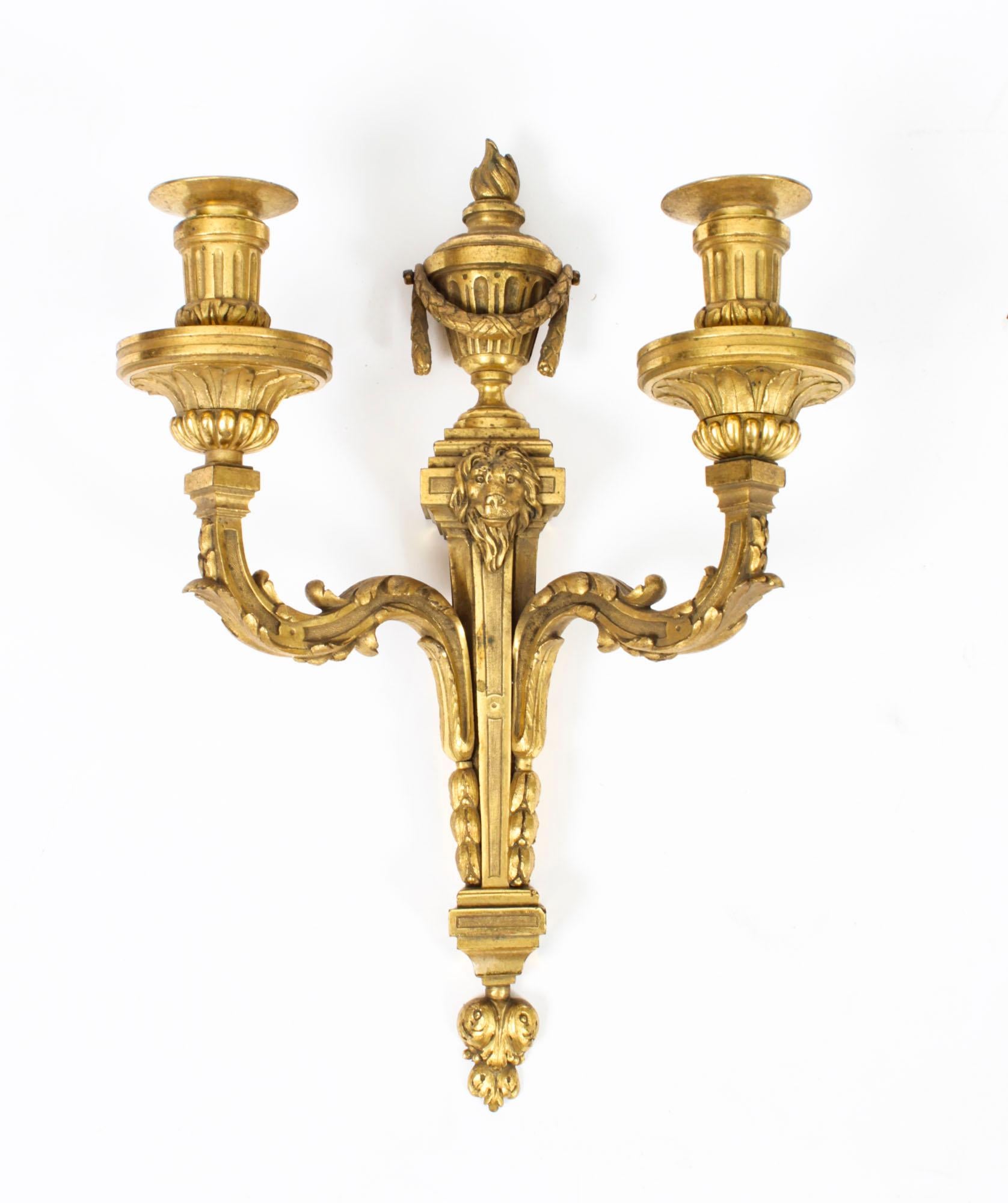 This is a fine pair of antique Regency Revival twin branch ormolu wall candle lights dating from Circa 1850.
 
The wall lights feature torch urn shaped tops above tapering bodies with lions mask mounts, each with acanthus leaf cast shaped branch