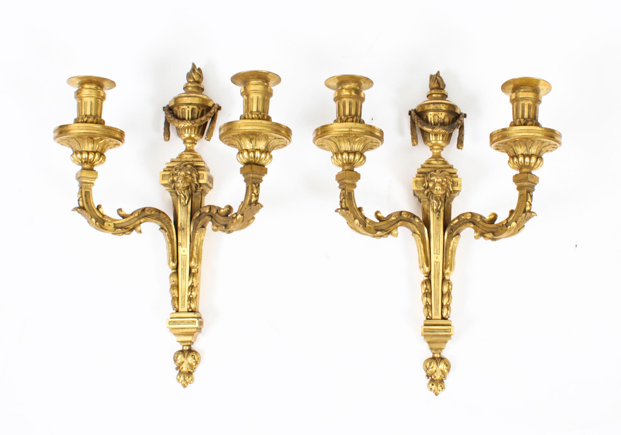 This is a fine pair of antique Regency Revival twin branch ormolu wall candle lights dating from Circa 1850.

The wall lights feature torch urn shaped tops above tapering bodies with lions mask mounts, each with acanthus leaf cast shaped branch arms