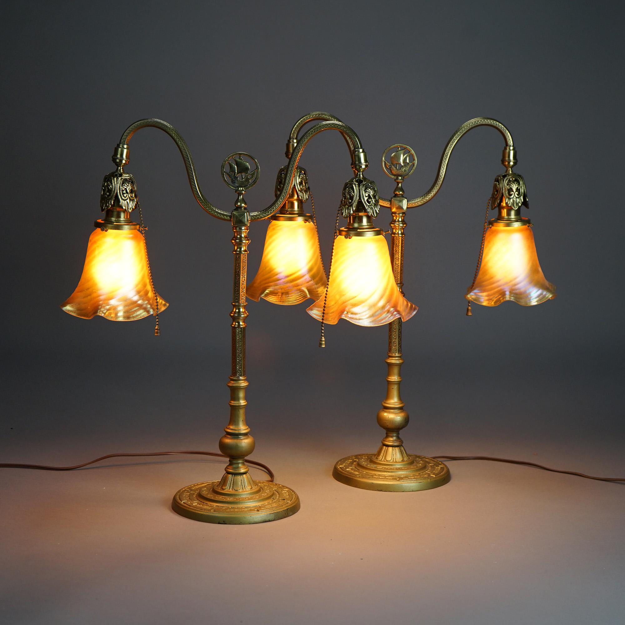 An antique pair of bankers lamps in the manner of  Rembrandt offer gilt cast  brass bases with scroll form double arms having central ship finials and terminating in art glass shades; embossed foliate designs throughout, c1920

Measure - 20.5