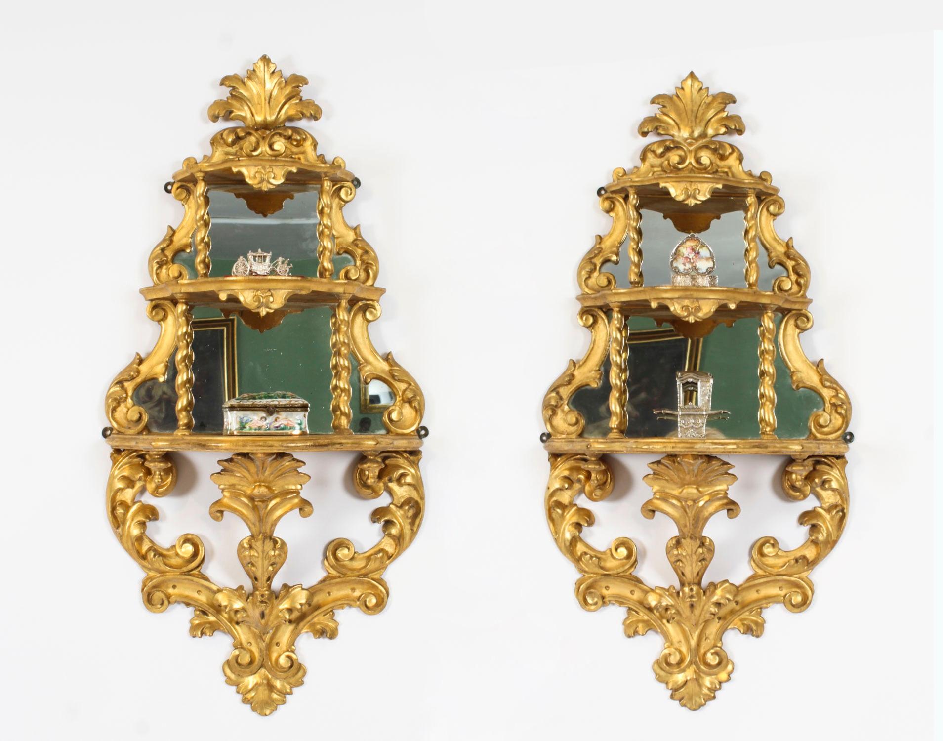 Un'elegante coppia di mensole a specchio da parete in legno dorato in stile Rococò, datate circa 1880.

Presentano stemmi a conchiglia stilizzati sopra due ripiani con grembiule a cartiglio,

La cornice in acanto a volute intagliate e conservano la