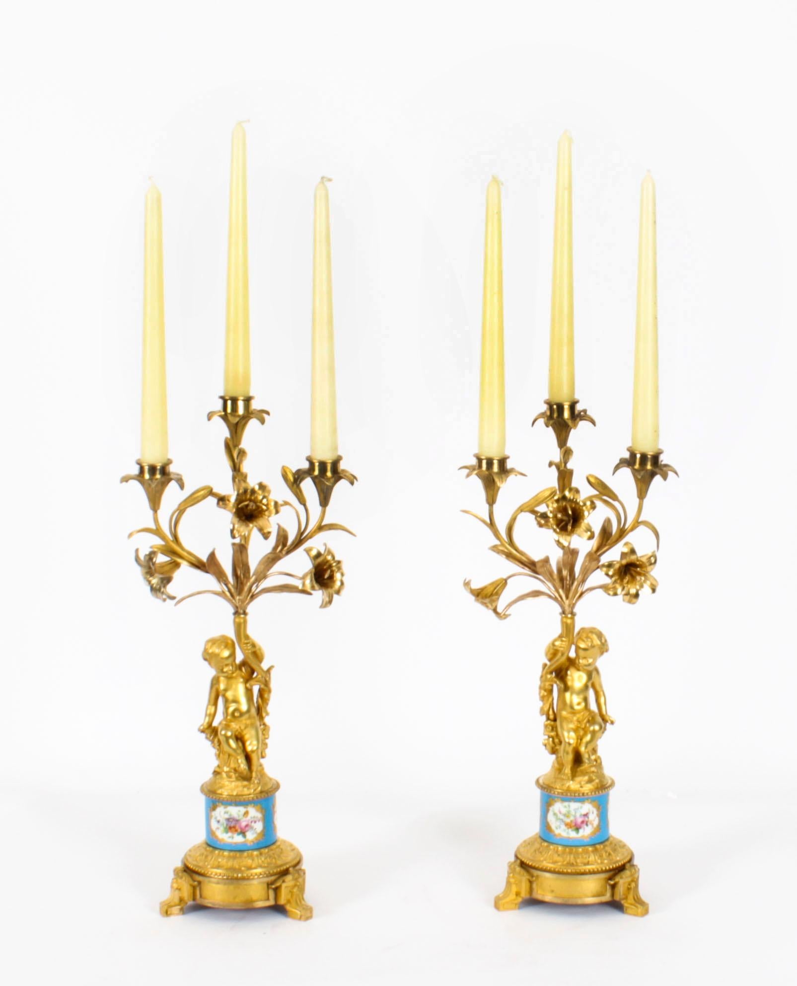 Ein Paar französischer Porzellan- und Ormolu-Kandelaber des späten 19. Jahrhunderts mit drei Lichtern, jeweils mit floralen und blattförmigen Zweigen über einer cherubischen Mittelsäule, auf einem floral bemalten Porzellankragen und einem