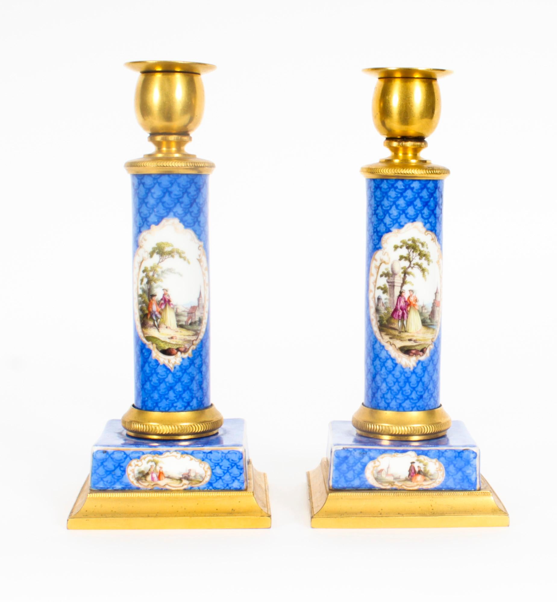 This is a delightful antique pair of 19th century French Sevres porcelain mounted ormolu candlesticks, C1870 in date.
 
The square bases and plain column stems with tulip sconces decorated with romantic classical landscape panels on a blue scale