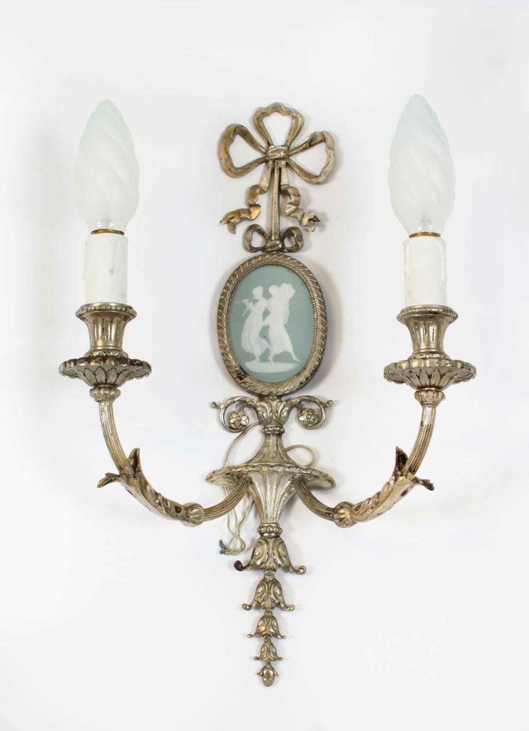 Si tratta di una splendida coppia di lampade da parete a due rami in ormolu e porcellana, risalenti al 1900 circa,

Di elegante forma classica con bracci a nastro ribaltati con decorazione ad acanto e appliques foliate, ogni piastra posteriore è
