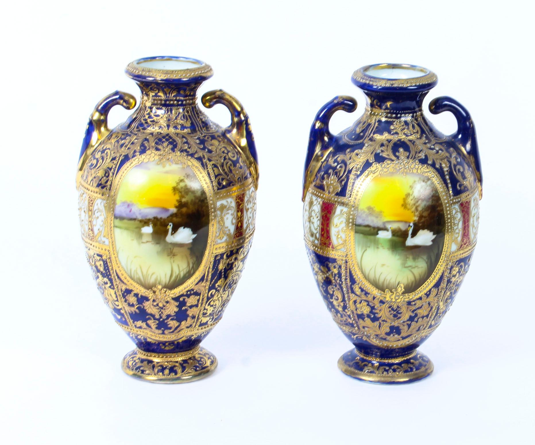 This is a beautiful antique pair of Taisho Period hand painted twin handled Noritake porcelain vases painted with swans, circa 1920 in date.

They feature attractive multi coloured floral patterns with a dominant navy blue background. 

Instill