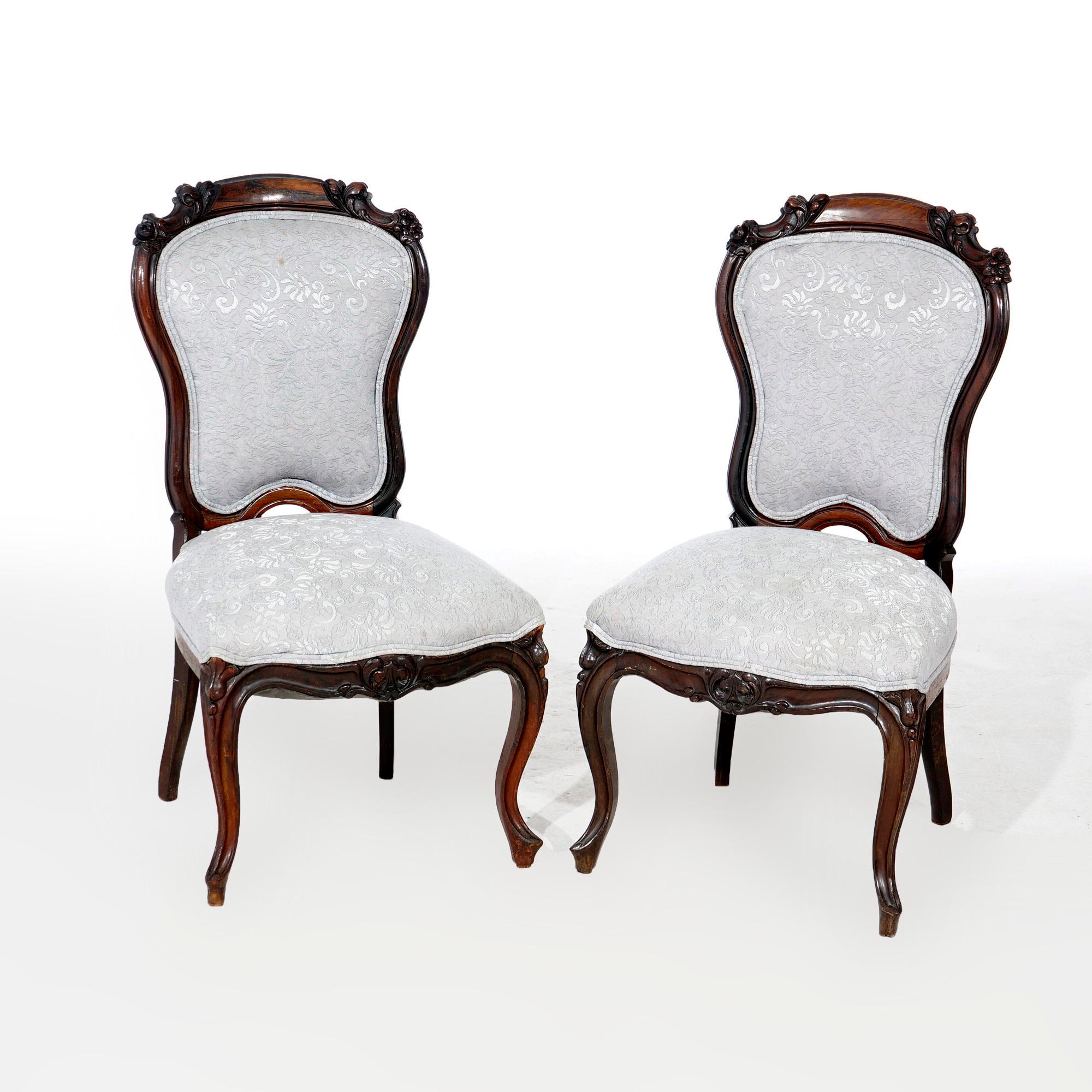 An antique pair of Victorian parlor side chairs offer mahogany construction with carved foliate elements, upholstered backs and seats, raised on cabriole legs, 19th century.

Measures- 36.25''H x 19.25''W x 21''D; 19'' seat height.
