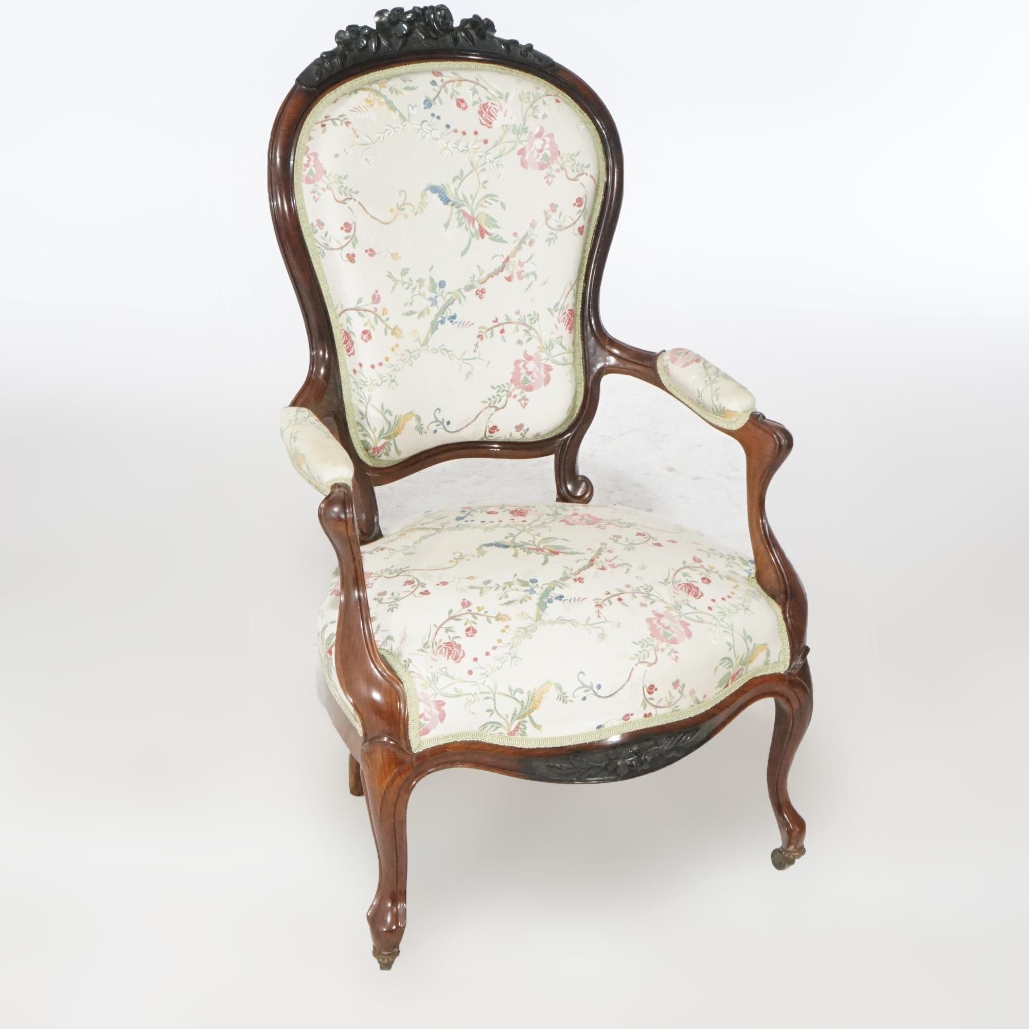 An antique pair of Victorian parlor armchairs offer rosewood construction with carved floral crest over upholstered seat, arms and backs, raised on cabriole legs, c1890.

Measures- 41.5''H x 25.25''W x 28''D.