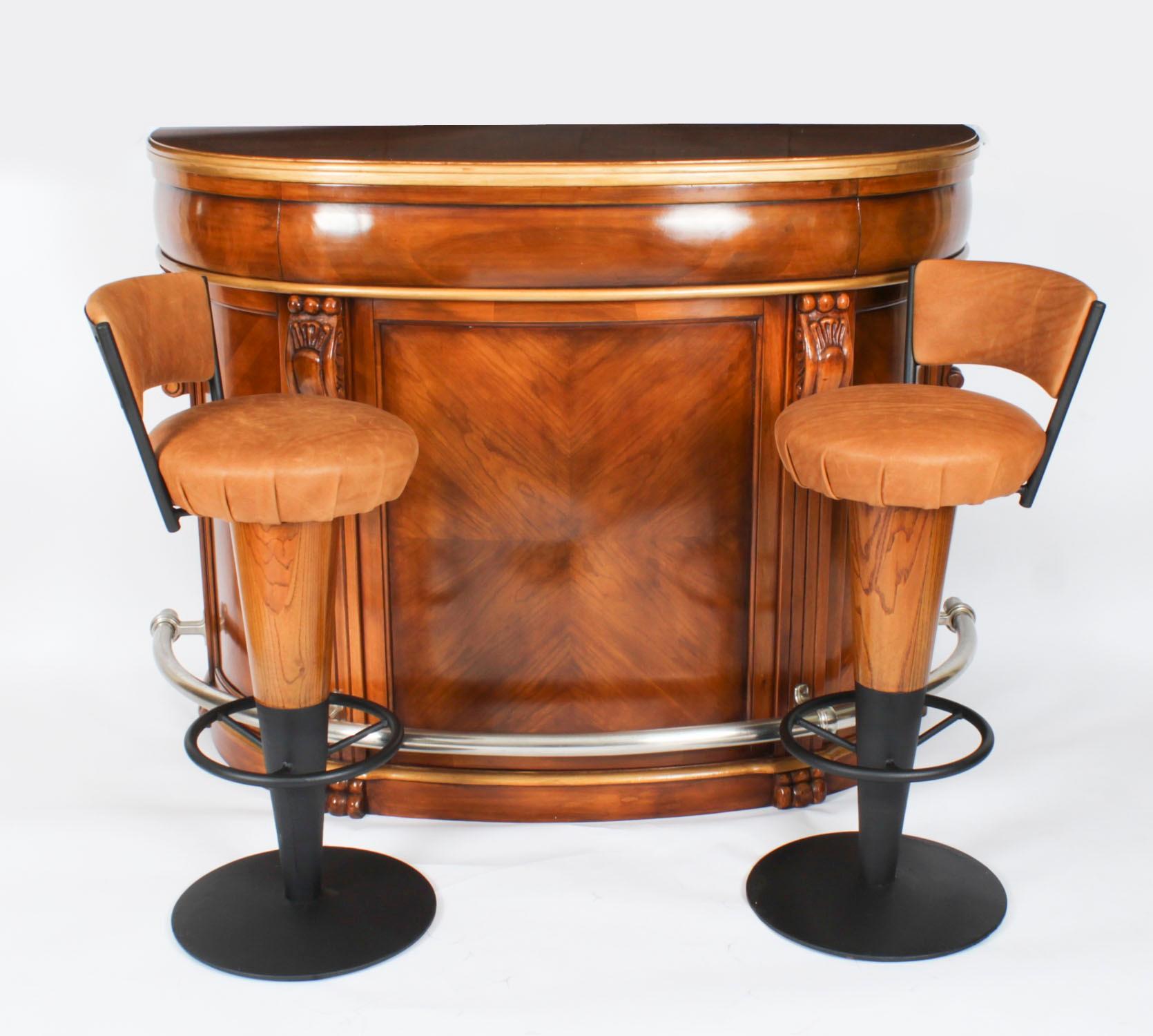This is a fabulous antique pair of Art Deco revolving bar stools that are made of  walnut with a black iron base, upholstered in tan leather, and dating from the first half of the 20th century.

Each has a foot rail and they have sumptuous leather