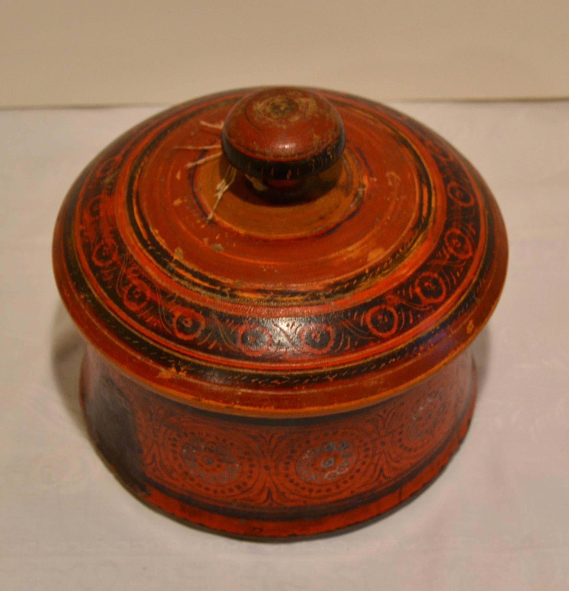 This is a delightful medium-size hand-turned, incised and hand-painted antique tribal wooden spice box from Pakistan, with a red and black pattern of concentric circles and wheels. Its multiple chips, scrapes, and dings, and one significant candle