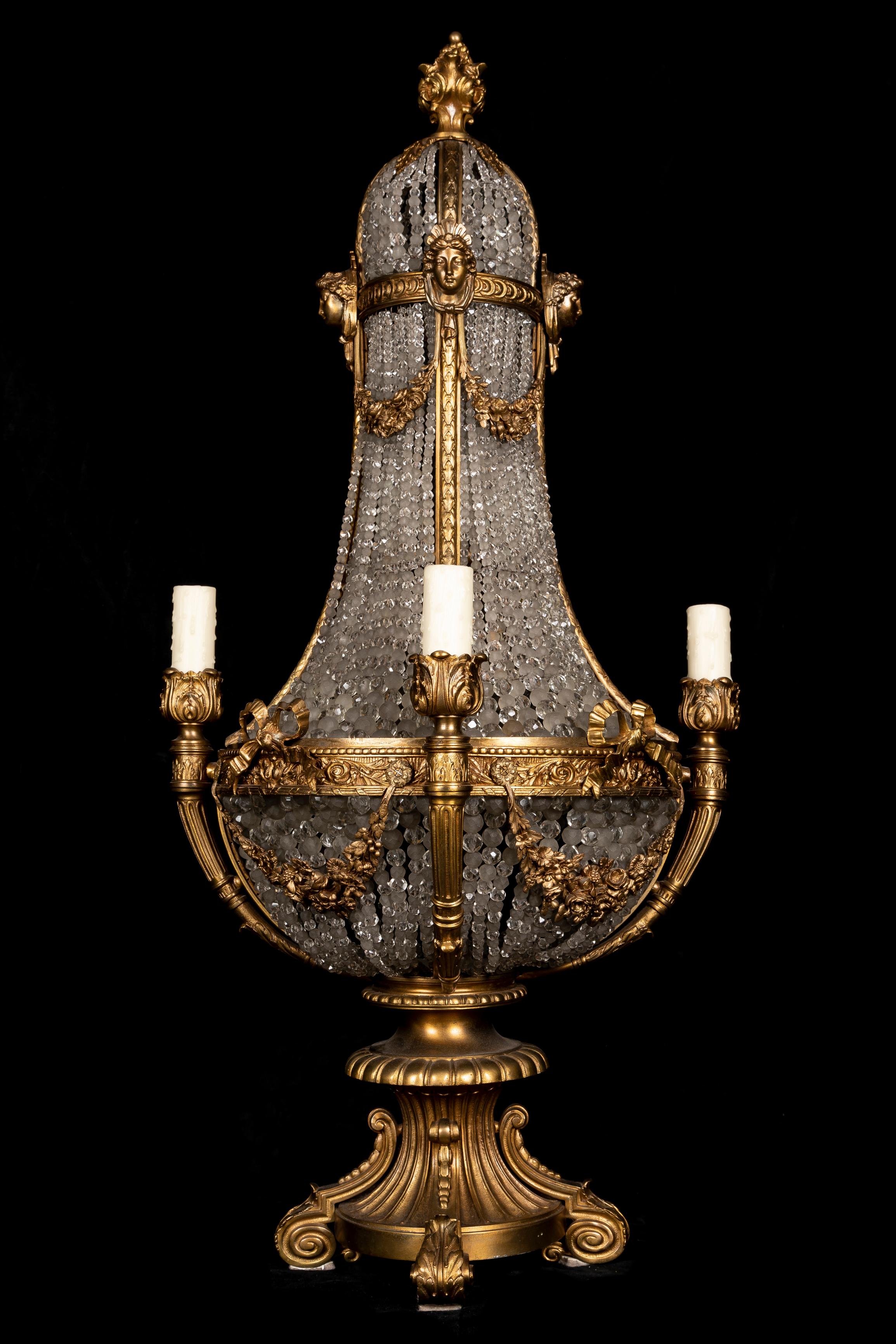 This large Palatial Antique French Louis XVI-style chandelier lamp, of palatial size, features a gilt bronze frame adorned with neoclassical motifs and cut crystal elements. The structure follows a baluster-shaped design, with an upper domed section