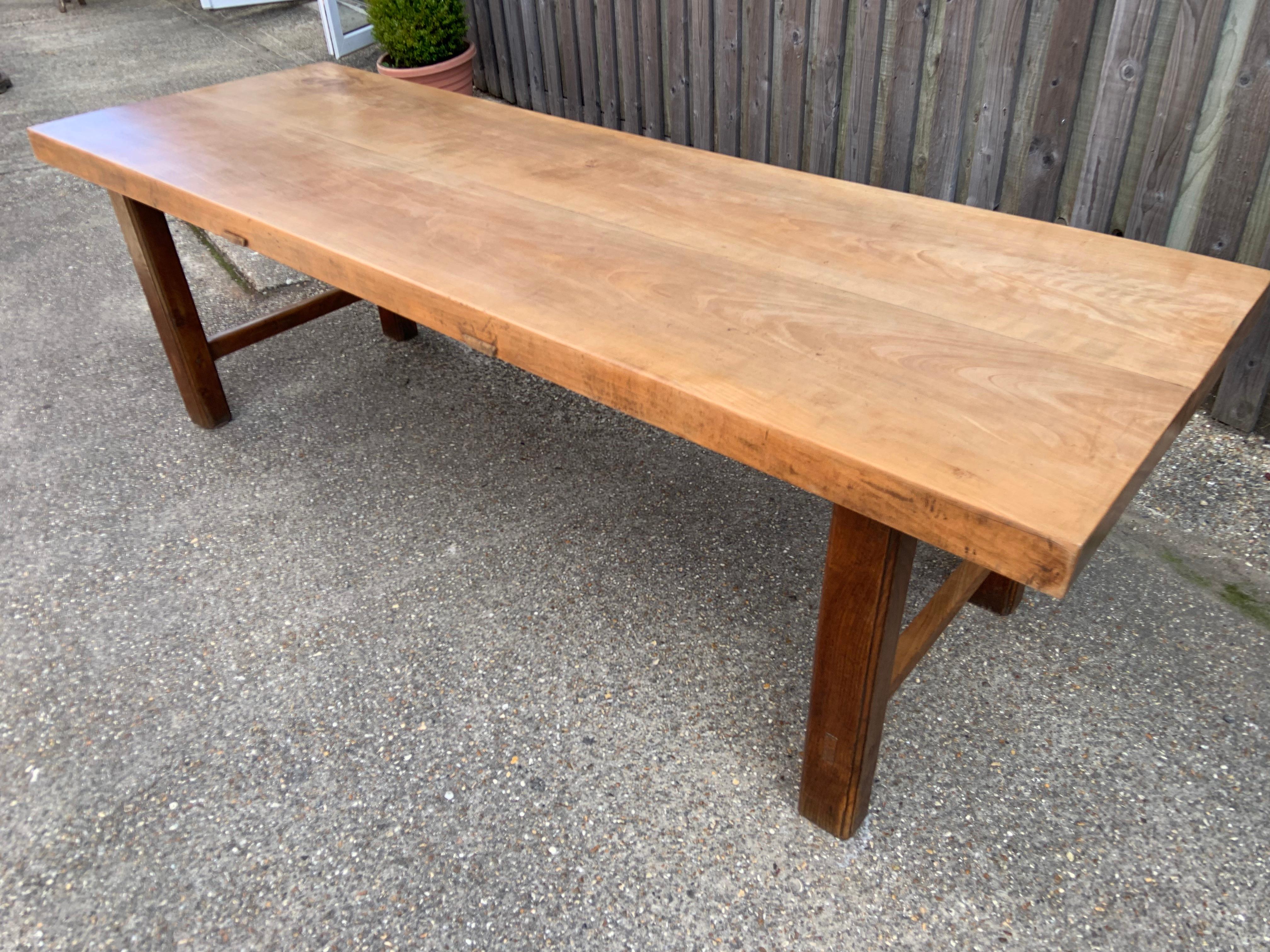 Table de ferme ancienne en hêtre pâle avec deux plateaux rectangulaires en planches épaisses. La table repose sur quatre pieds carrés et robustes, unis par un support en forme de H. Le plateau de la table a une épaisseur de 3 pouces et est d'une