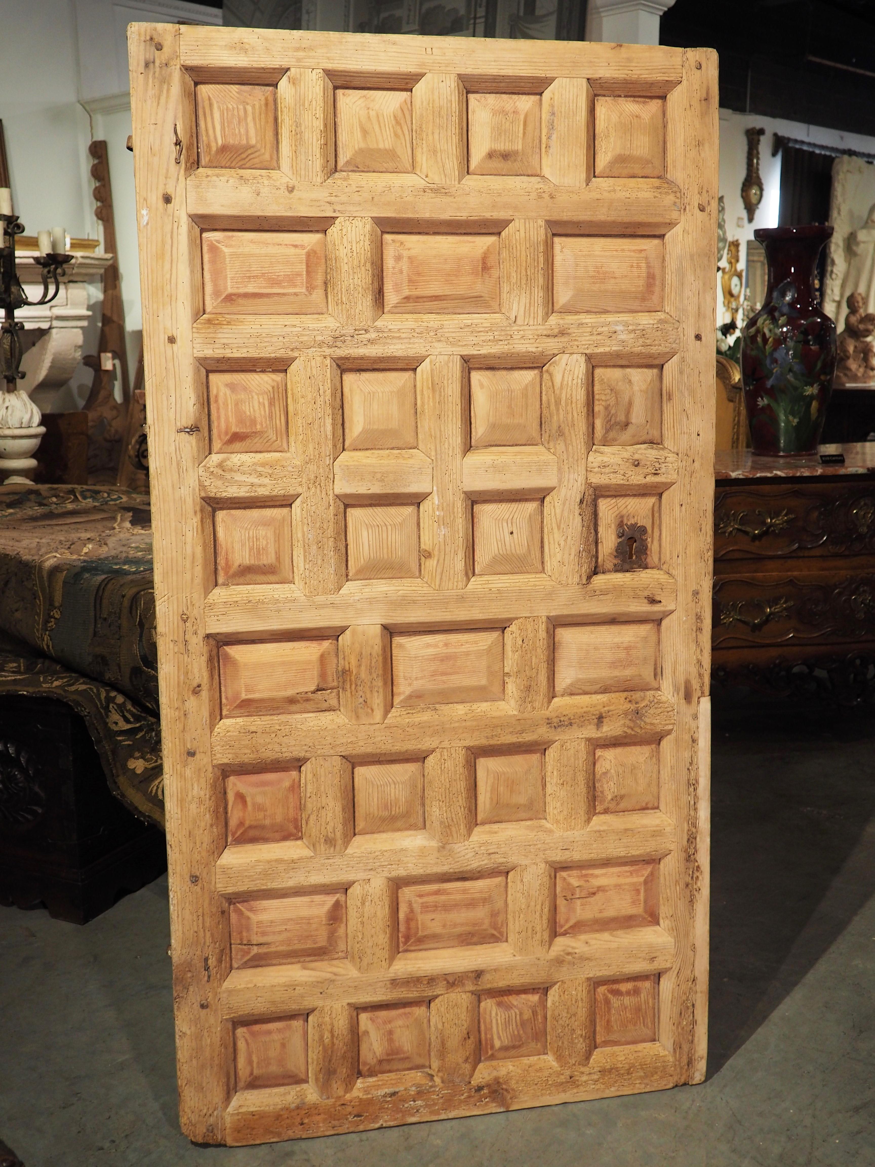 Hand-carved in Spain during the 1800’s, this antique farm door has eight rows of rectilinear panels assembled using mortis construction. Most of the panels are square, but there are a few rows of horizontally aligned rectangles. Each of the panels