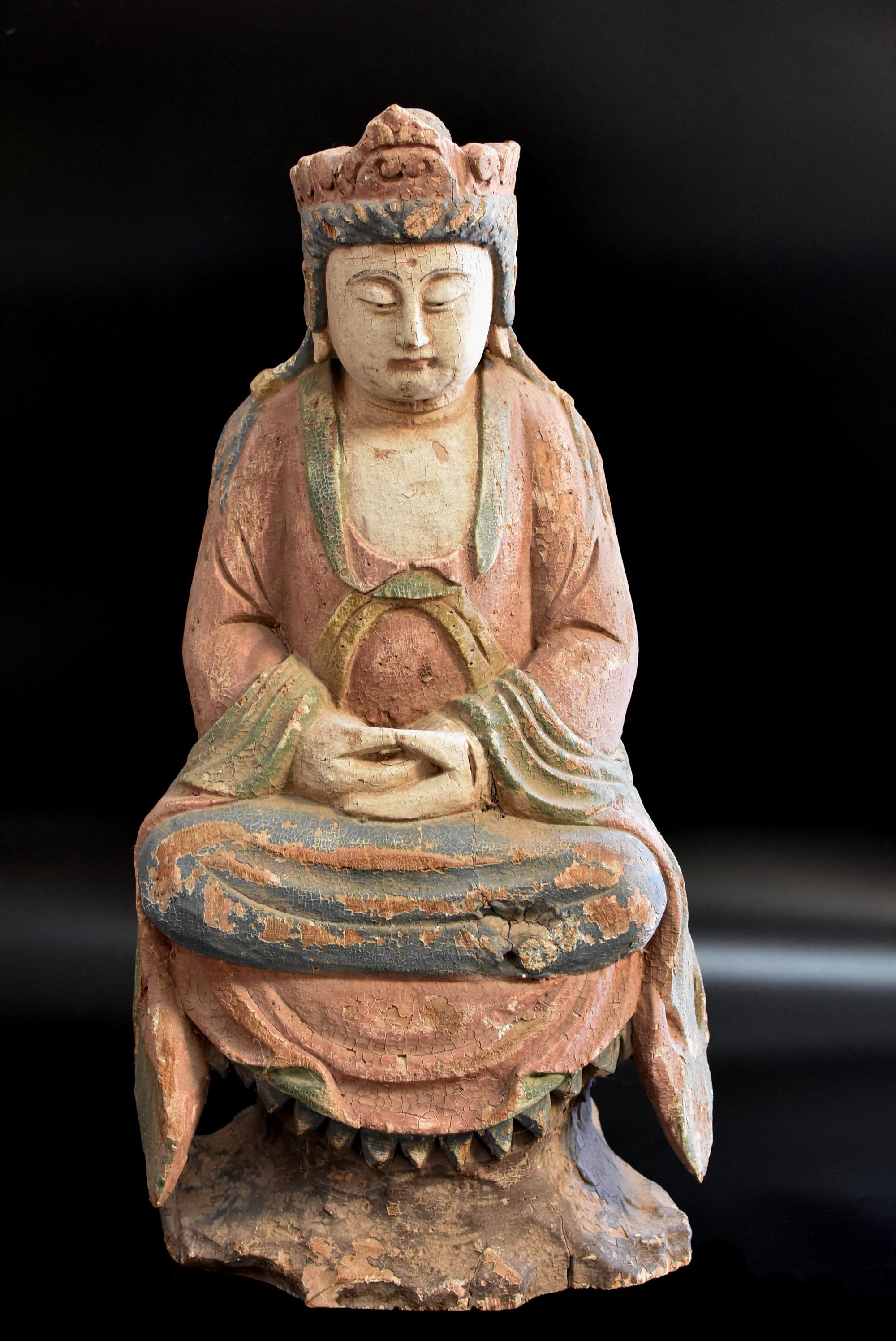 A large, early 20th century hand carved wooden statue of Kwan Yin in beautiful pastel color. Seated with her legs folded into a lotus pose on a high pedestal, Kwan Yin has a broad face with a serene expression, the almond-shaped downcast eyes