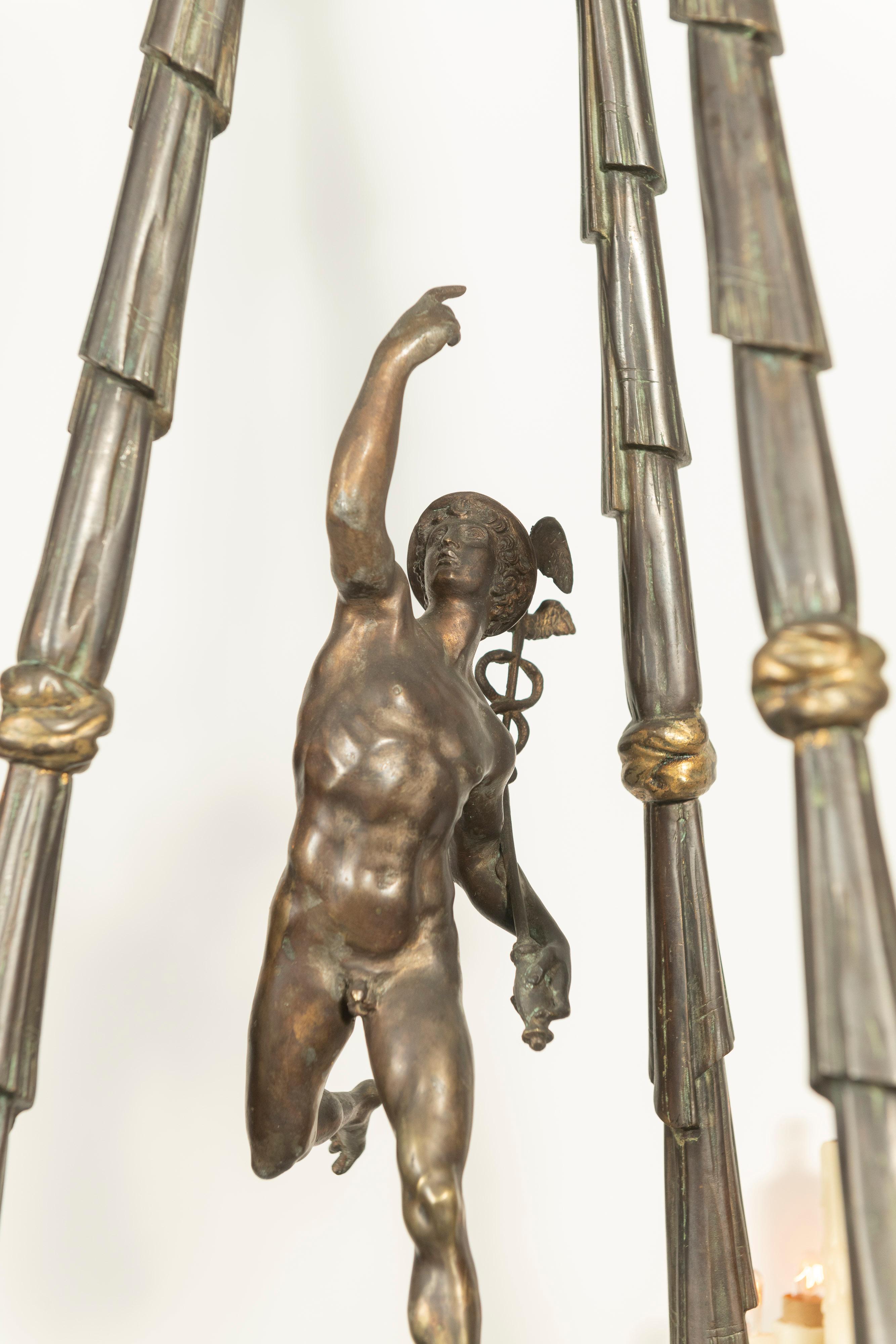 Dieser wunderschön gearbeitete Kronleuchter aus patinierter Bronze ist wirklich prächtig. Mit der detaillierten Figur des Merkur, Bronzegirlanden, Cherubinen und Gazellen,  Die drei Arme halten jeweils fünf kerzenförmige Glühbirnen. Die Leuchte ist