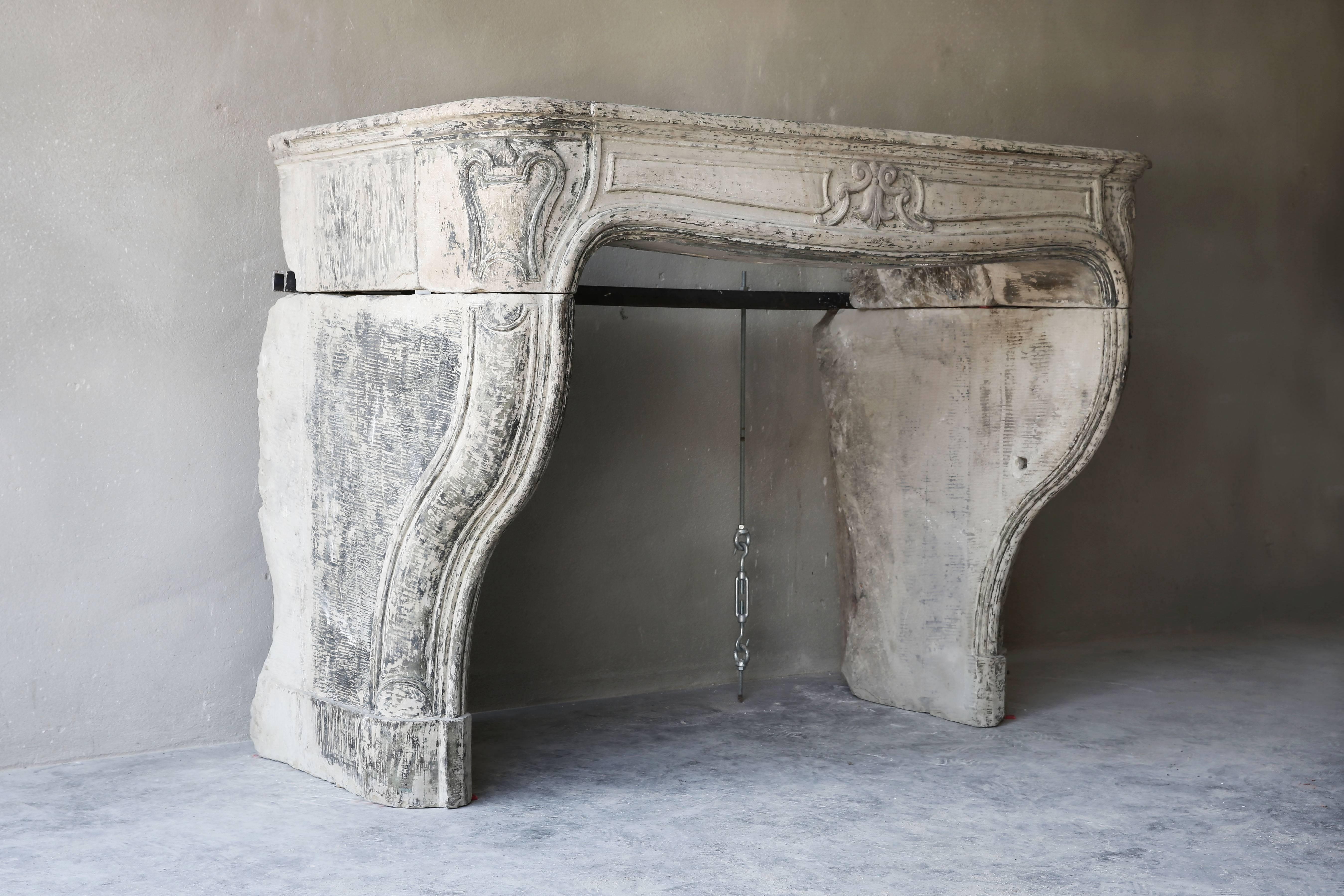 Very unique antique limestone fireplace with nice ornaments in the front section running on the legs. This particular fireplace fits into many interiors. The fireplace dates from the time of Louis XIV and the round shapes and patina gives the