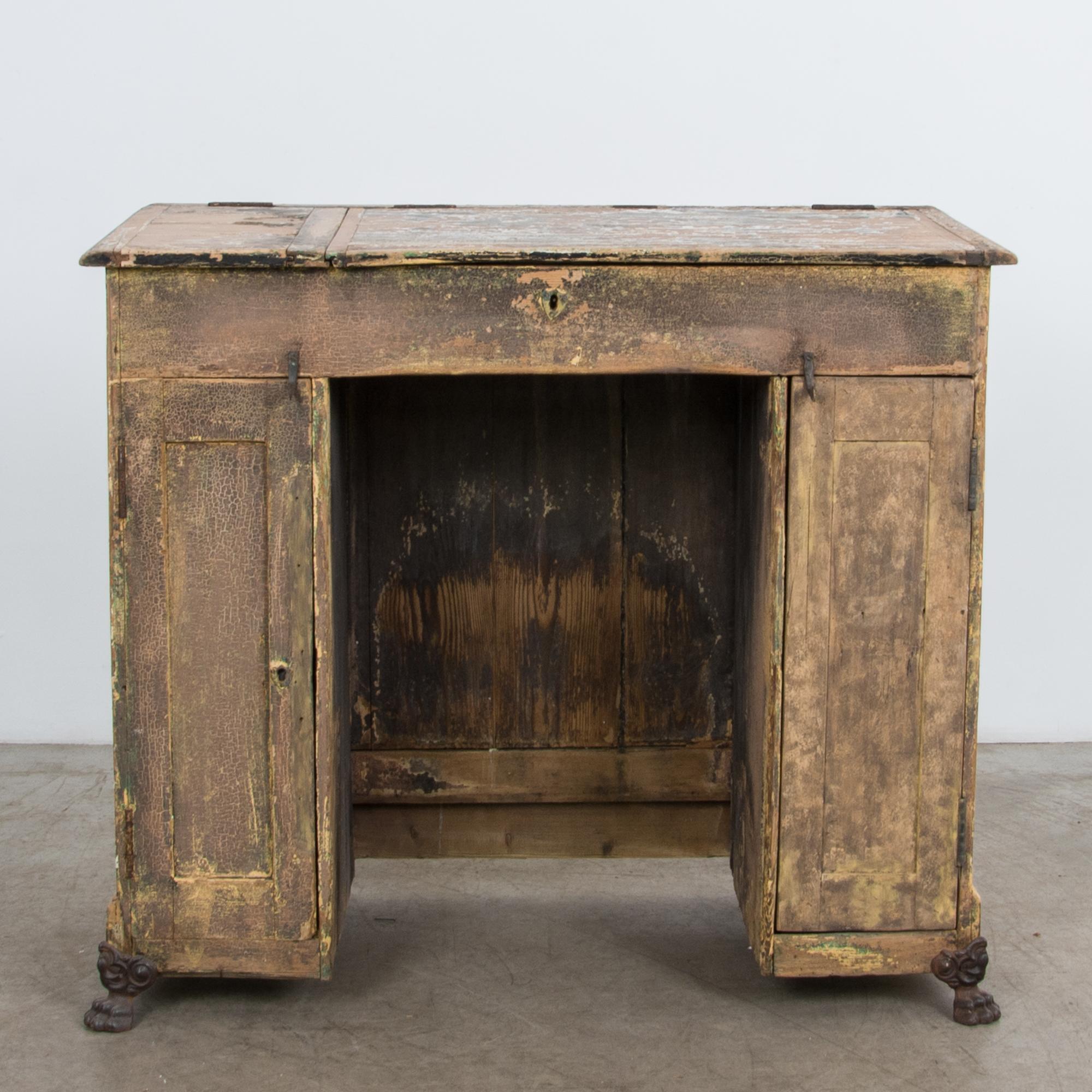 A compact desk with flip top storage space and two doors. From turn of the century France, a beautiful rustic patina is complimented by wrought iron hardware and cast iron clawfeet. Charming construction follows the tradition of regional French