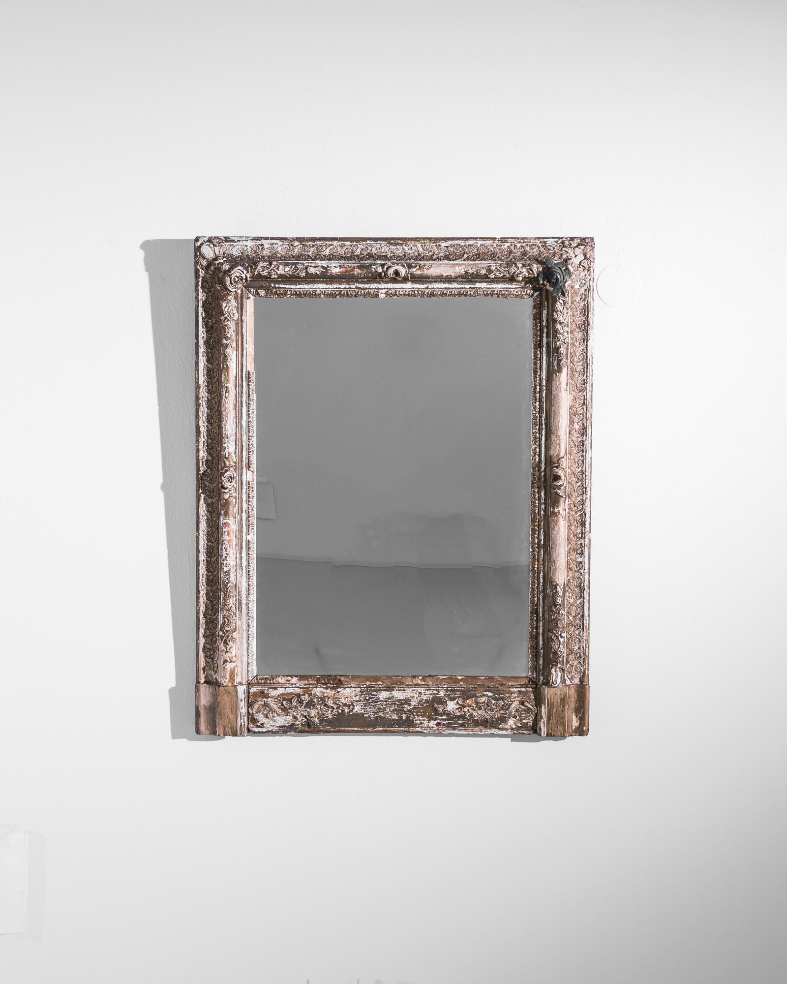 A white patinated wood framed mirror from France, produced circa 1900. A provincial french find is adorned with an evocative black rose, set in a deep frame of milky white wood. Chips in the original patination, and a sliver of silver backing, add