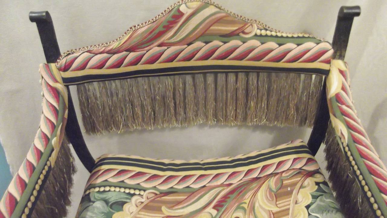 Dramática silla Savonarola de hierro con acabado en bronce.
El nuevo y colorido tejido está ribeteado con largos y fastuosos flecos en verde salvia.
Esta silla tiene una robusta y sólida estructura de hierro con una textura forjada a mano. Los