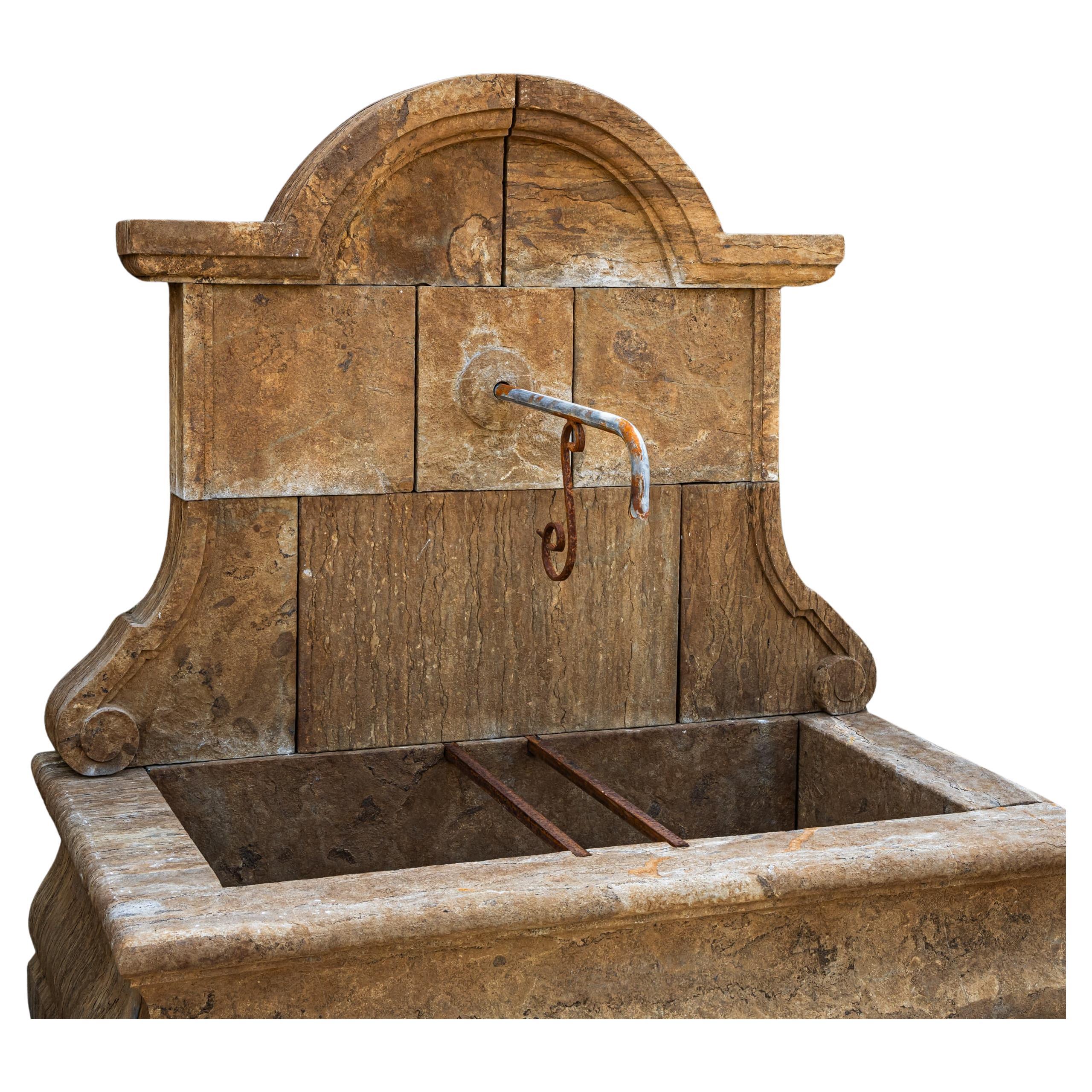 Fuente de pared de piedra natural patinada antigua, cincelada a mano, con una pila de líneas rectas y un panel posterior decorativamente curvado. El distintivo diseño en bloque y las sólidas proporciones garantizan una gran estabilidad y elegancia