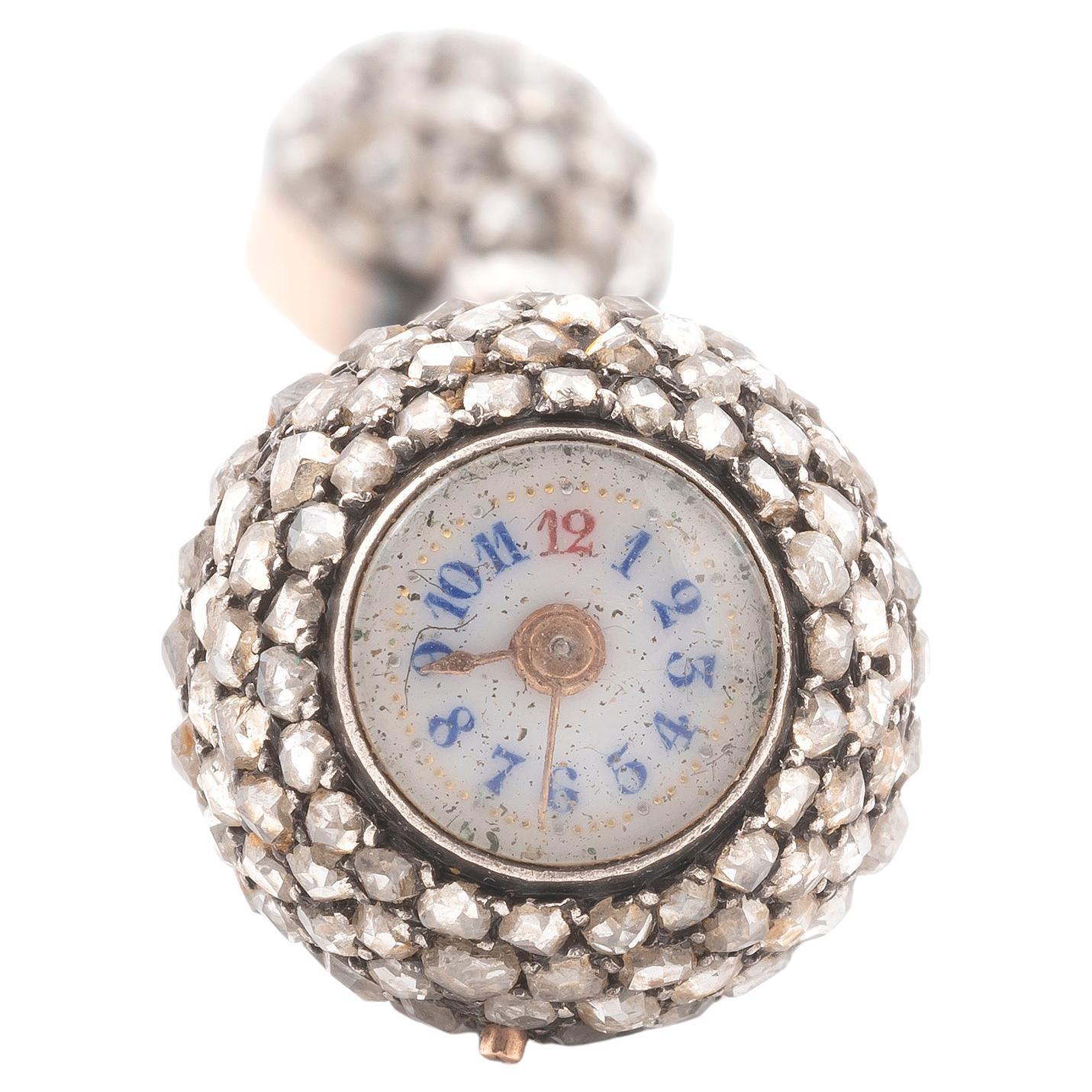Weißes Emailzifferblatt mit blauen und roten arabischen Ziffern, Lünettenaufzug und Zeigerfassung, spiralförmig angeordnete Diamanten im Rosenschliff, Anhänger mit Diamanten im Rosenschliff.
Mechanisches Uhrwerk mit Handaufzug durch Drehen der