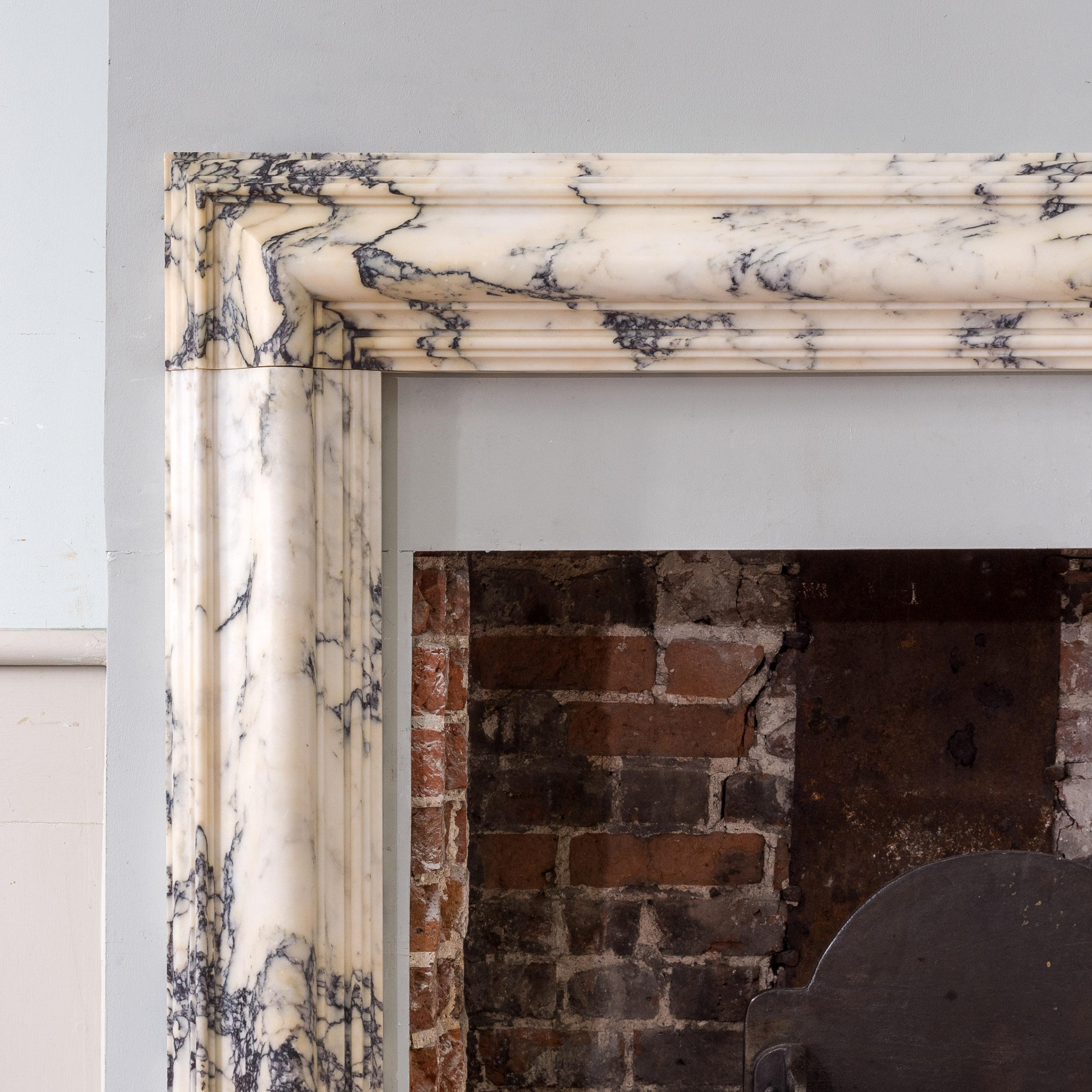 An antique Pavonazzo bolection fire surround in exceptionally figured material, early nineteenth century, the frame of ogee mould design raised on block feet.