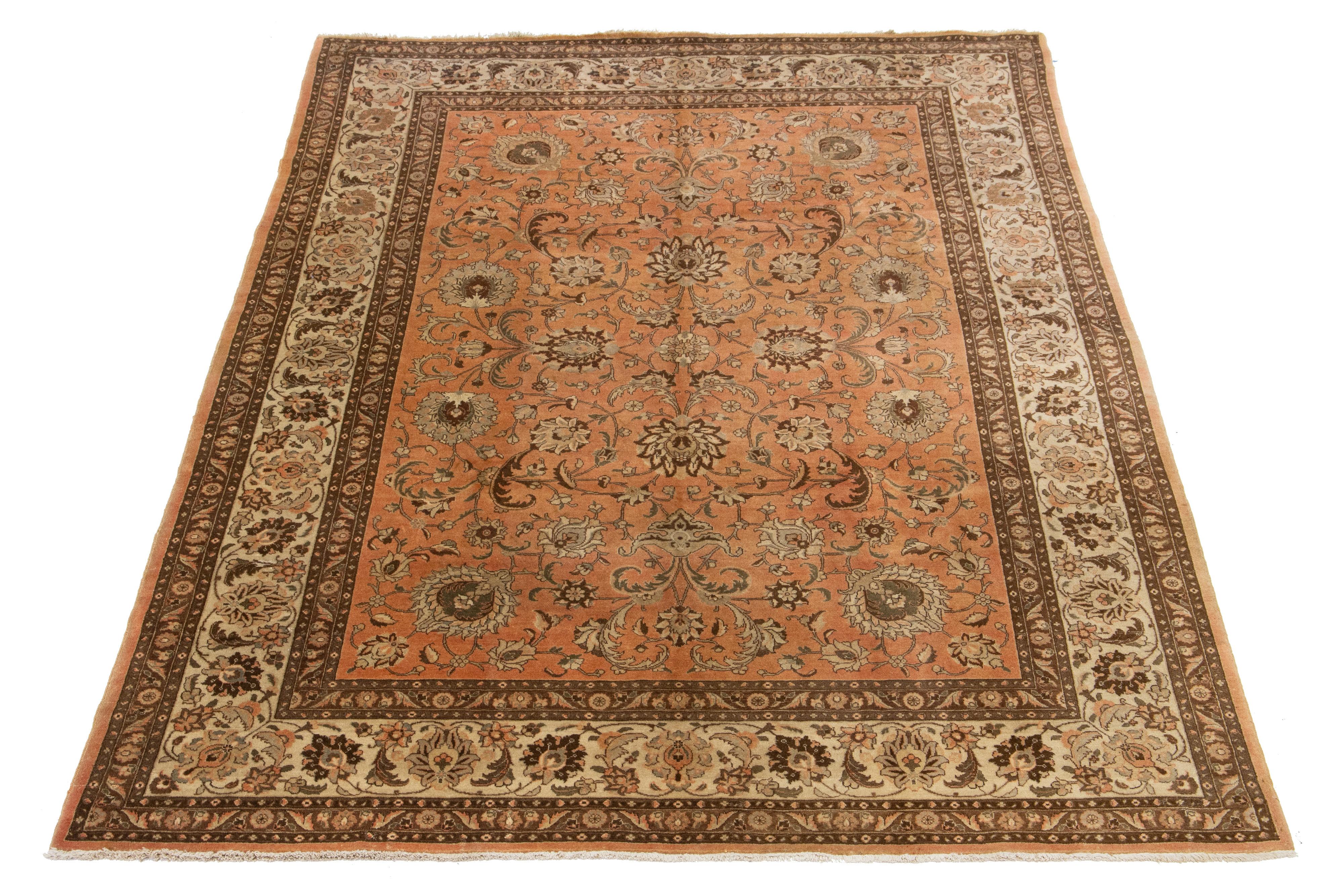 Dieser persische Wollteppich aus Täbris ist handgefertigt und zeigt ein klassisches florales Muster. Der pfirsichfarbene Hintergrund bildet einen Kontrast zu dem in Beige- und Brauntönen gehaltenen Design.

Dieser Teppich misst  8'8