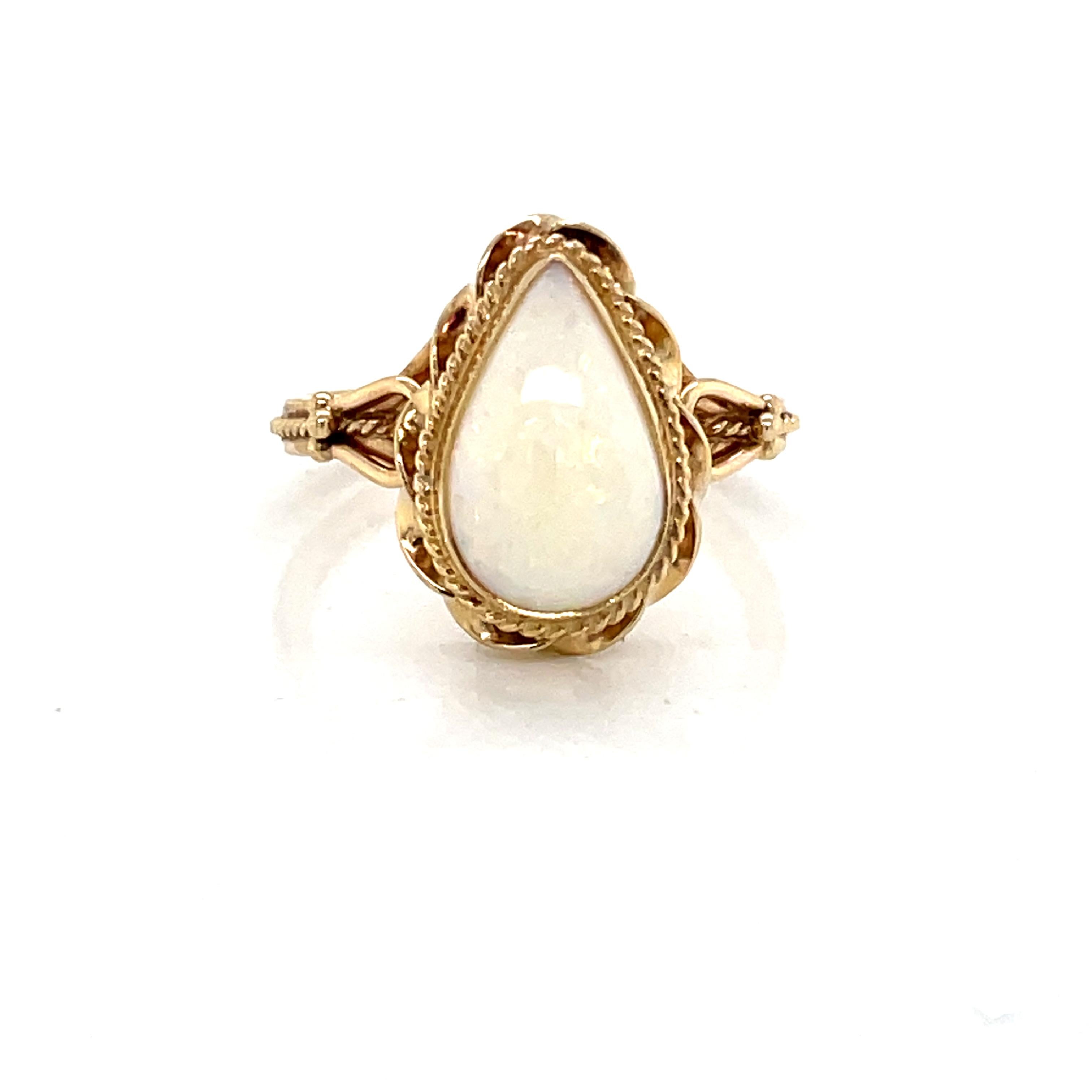 An elegant antique setting in fourteen karat yellow gold cradles the exquisite featured 8 x 4 mm pear shaped natural opal stone. Superb, with colorful iridescence, the opal gem stone is delicately framed with a fine twisted gold rope detail which